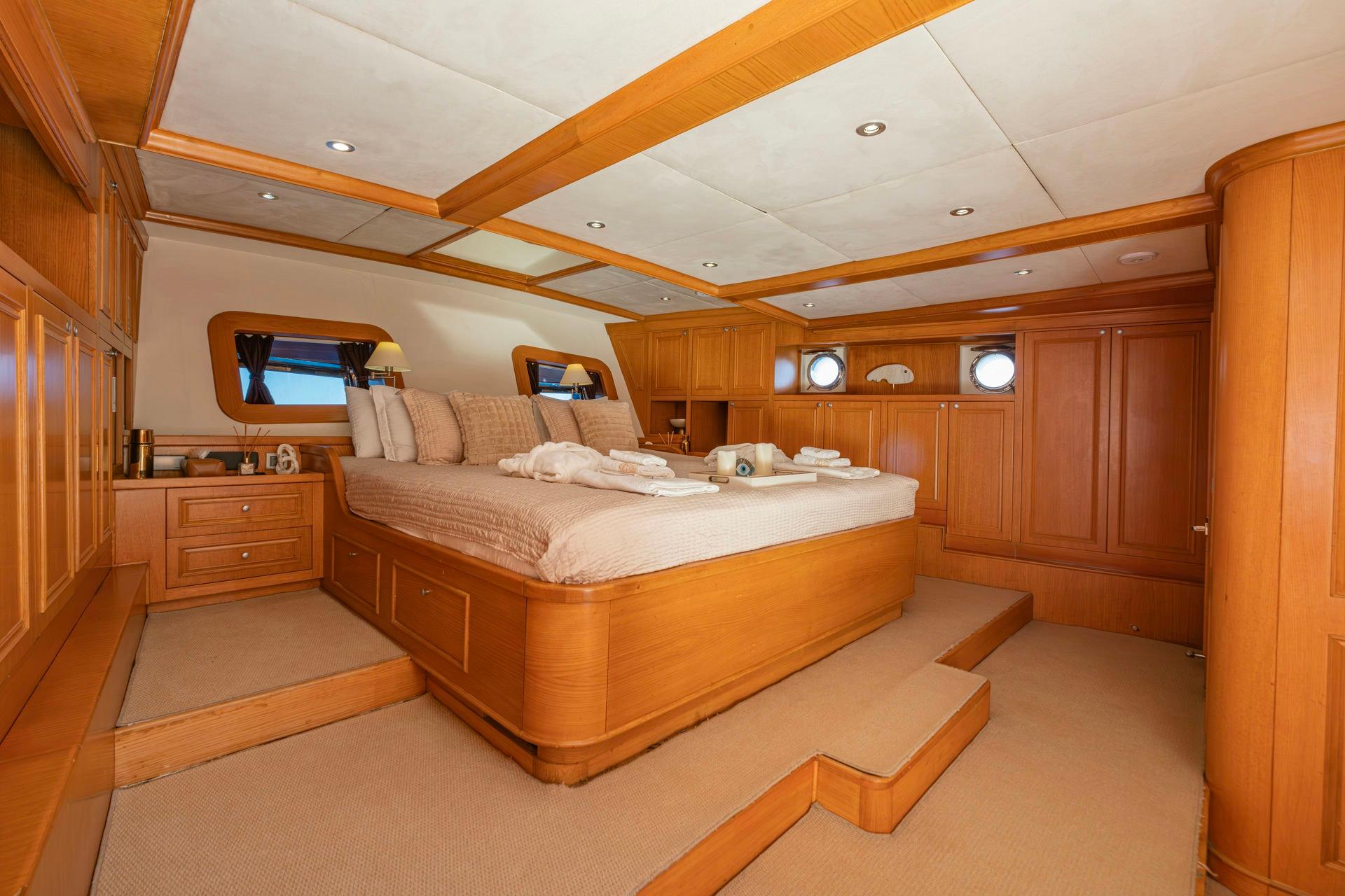 luxury yacht master cabin featuring king bed, wooden cabinetry, built-in storage and portholes