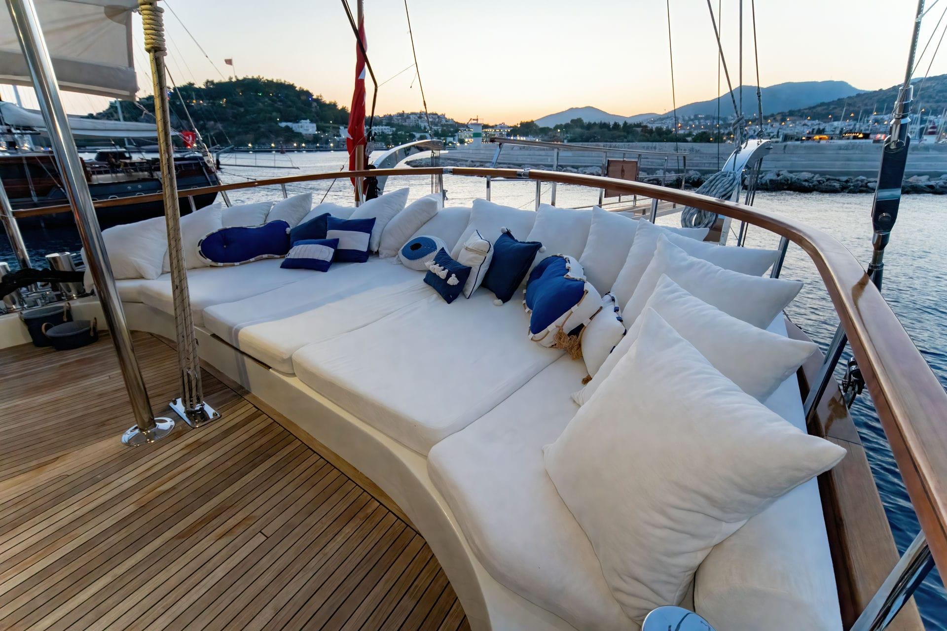gulet bow deck lounge area with white cushioned seating and blue accent pillows at marina