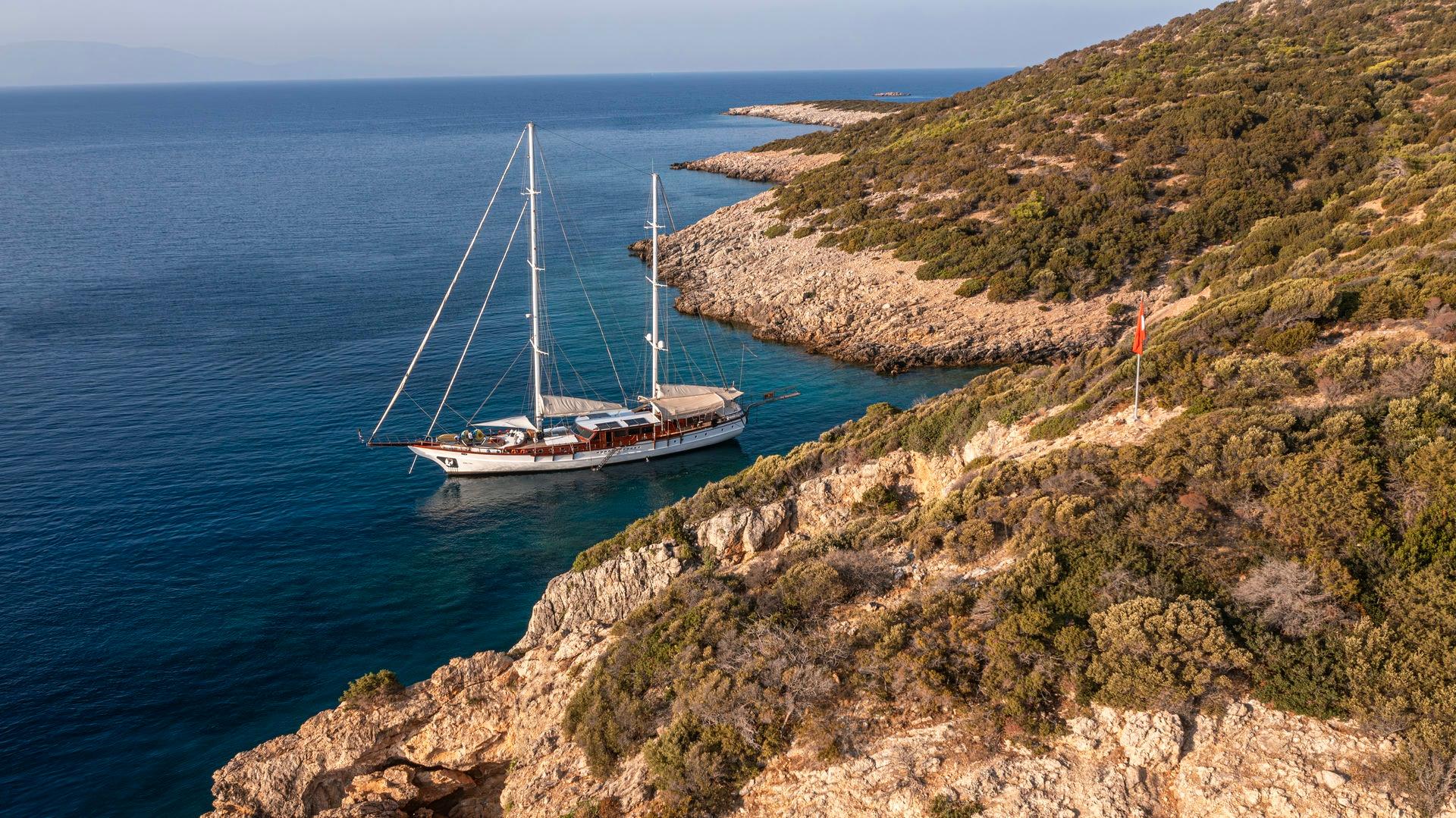aerial view of traditional wooden gulet yacht anchored in crystal clear turquoise bay surrounded by rocky coastline