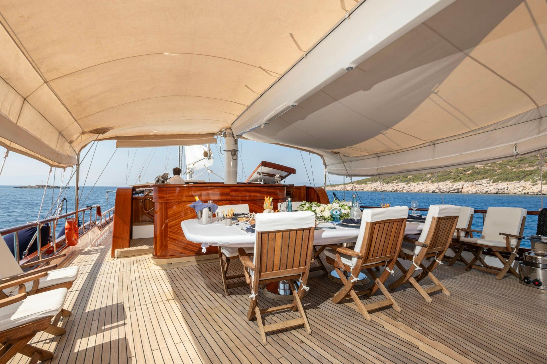 Gulet aft deck dining area with white table, teak chairs under canvas awning