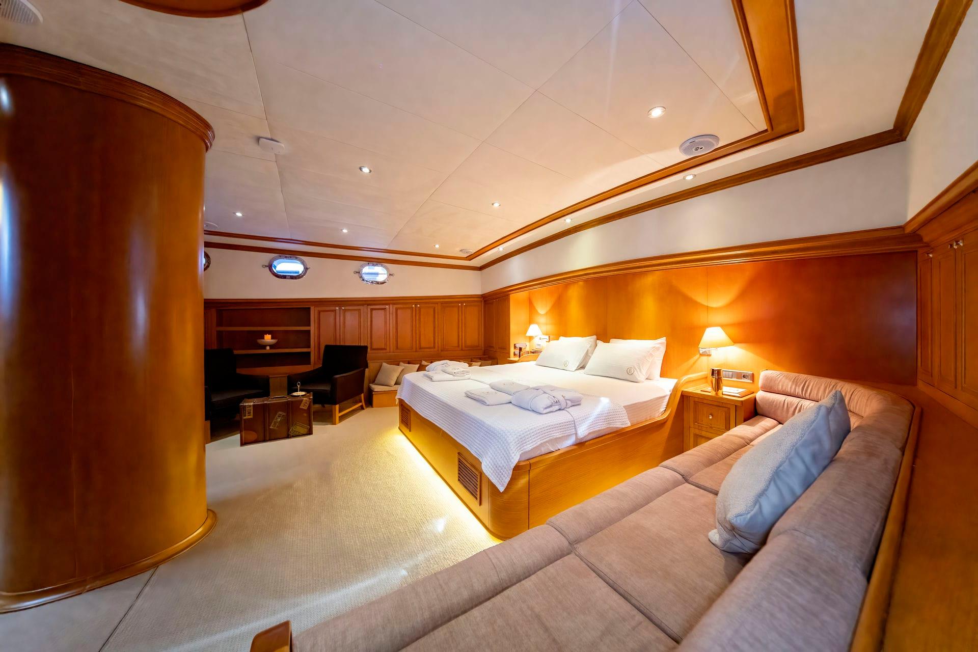 luxury yacht master cabin featuring king bed, beige sofa, entertainment center and portholes