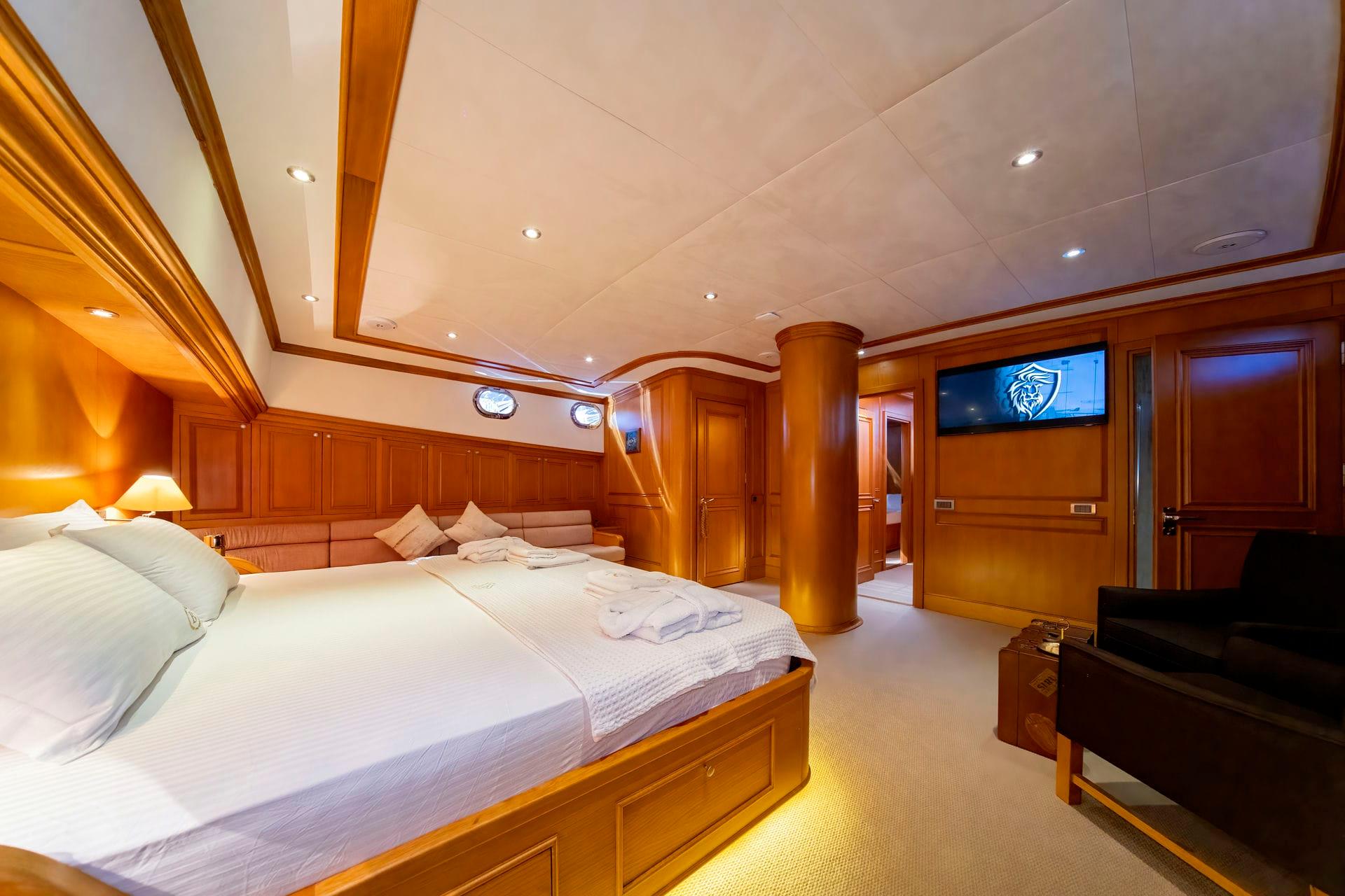 luxury yacht master cabin featuring king bed, built-in seating, wall-mounted TV and elegant wood paneling