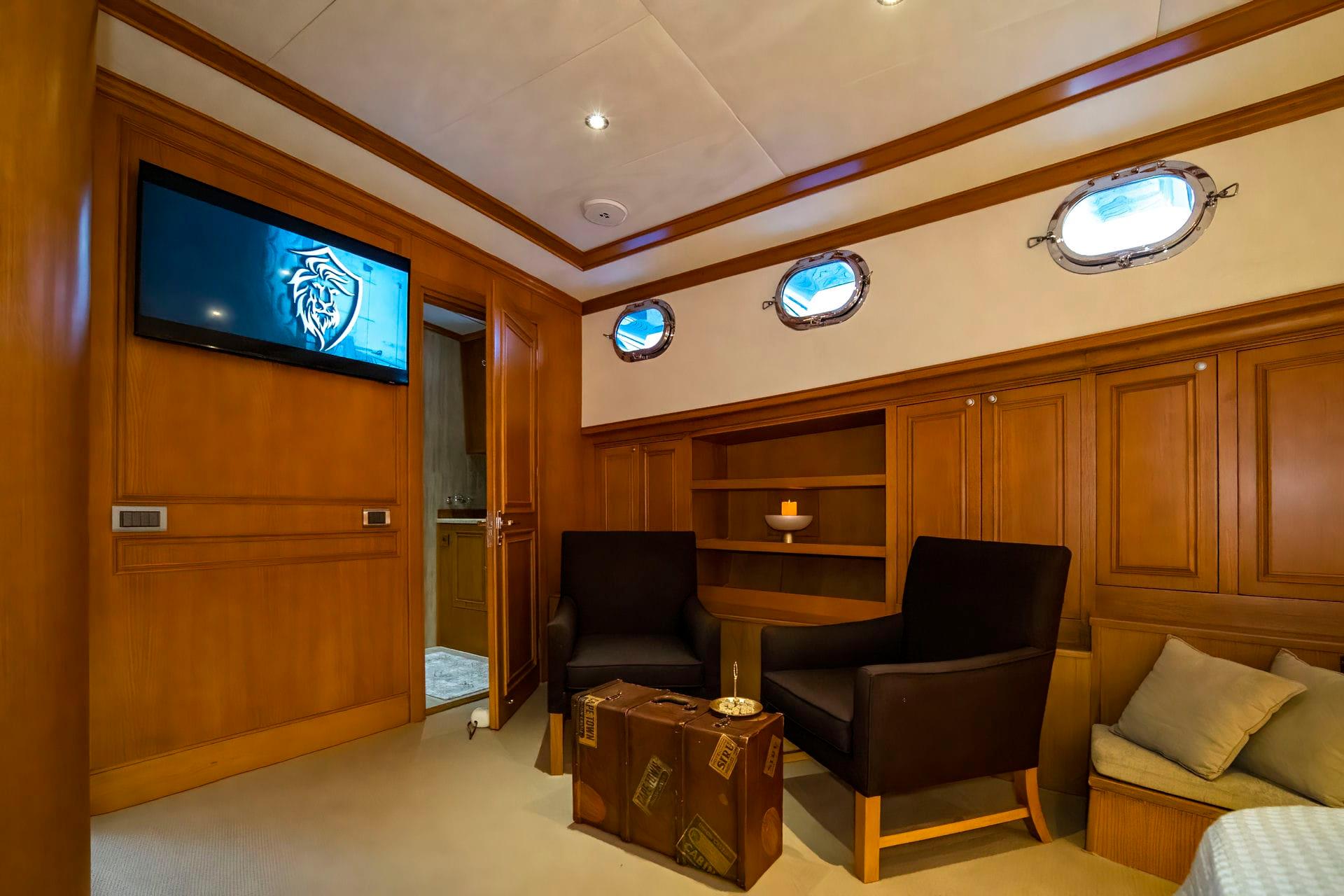 yacht cinema room with wall-mounted TV screen, black leather armchairs and wooden trunk coffee table