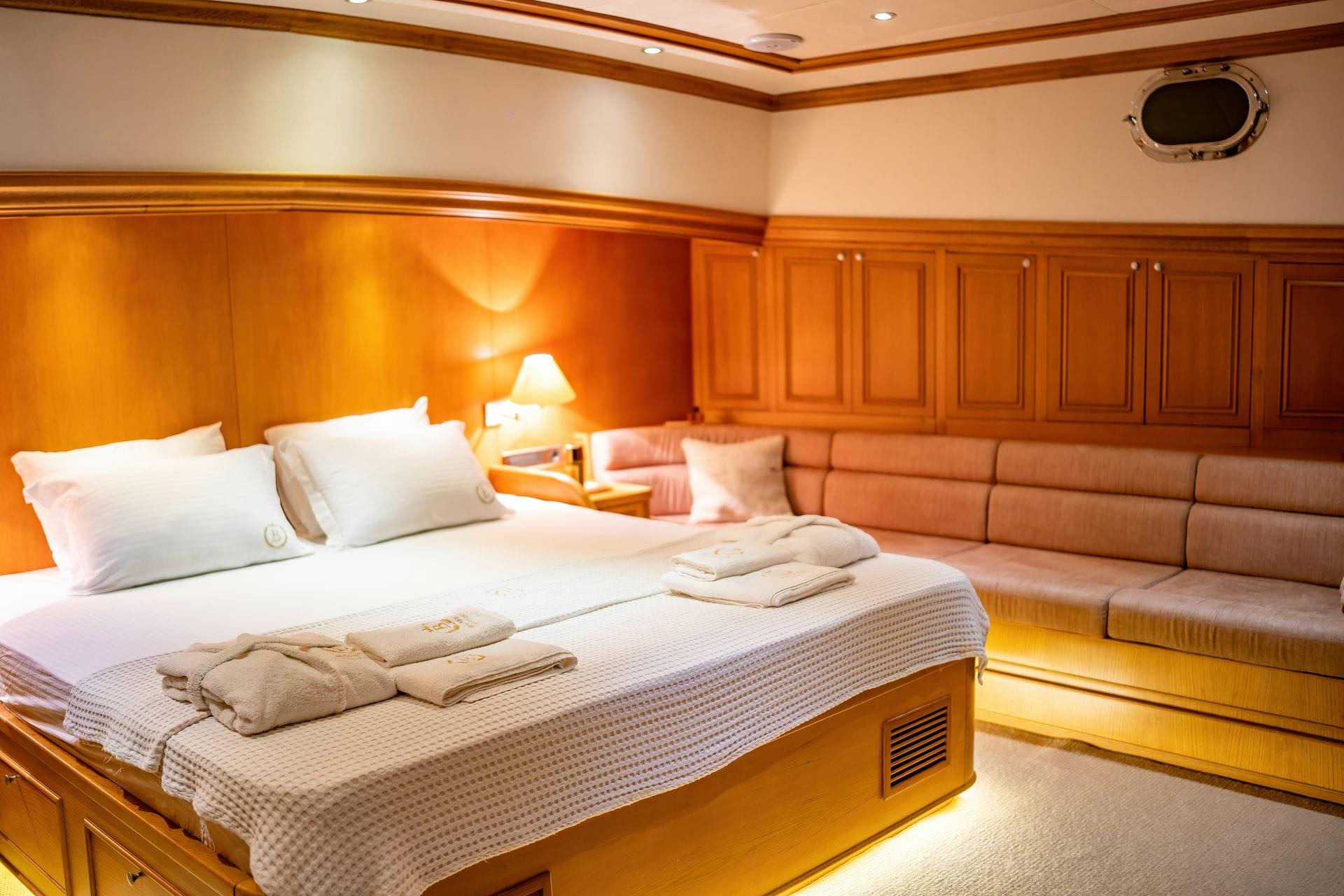 yacht cabin interior with double bed, built-in seating, wood paneling and porthole
