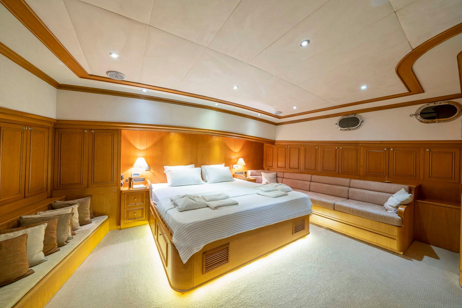 luxury yacht master cabin featuring double bed, built-in seating, wood paneling and portholes