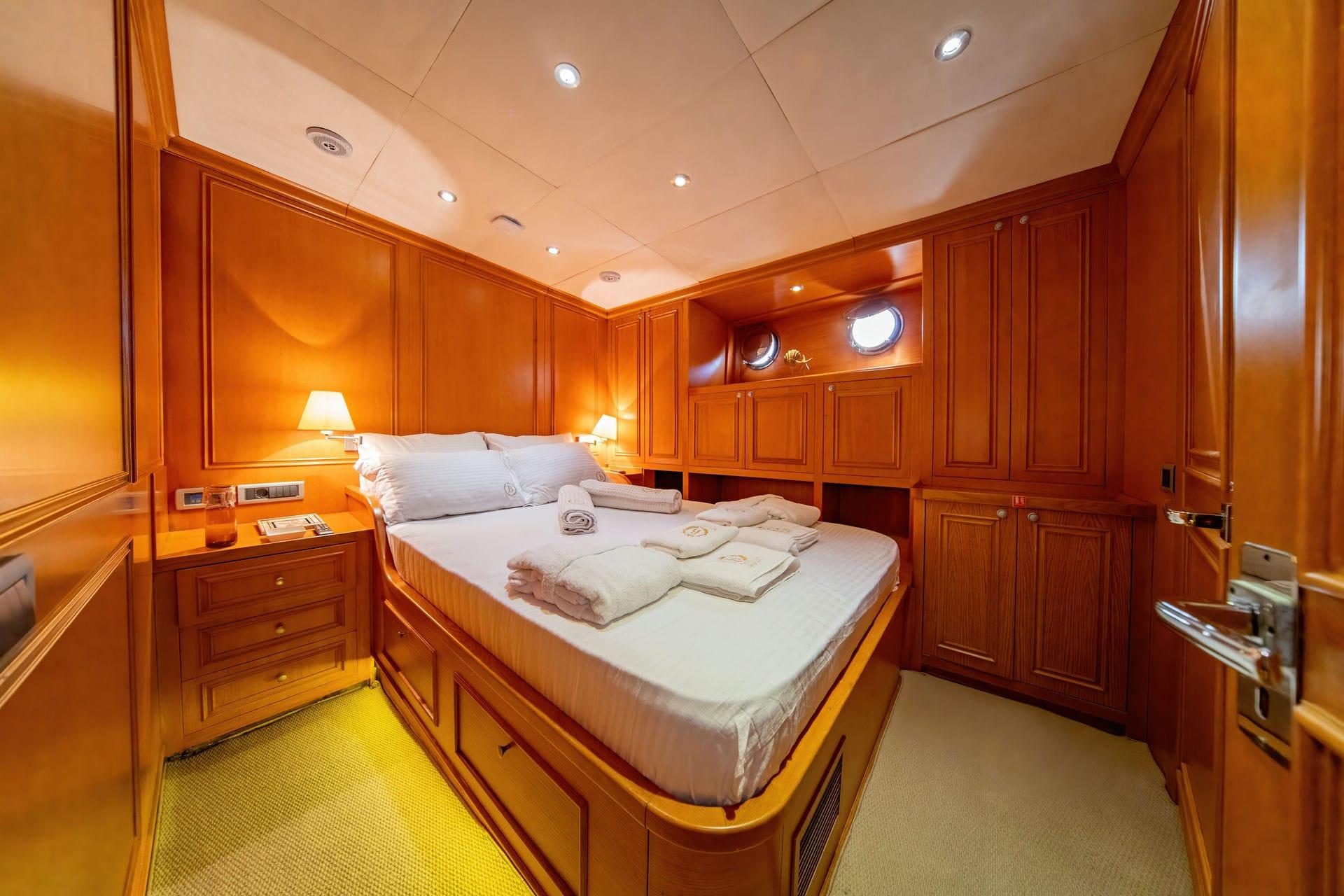 yacht guest cabin featuring double bed, rich wood paneling, built-in storage and portholes