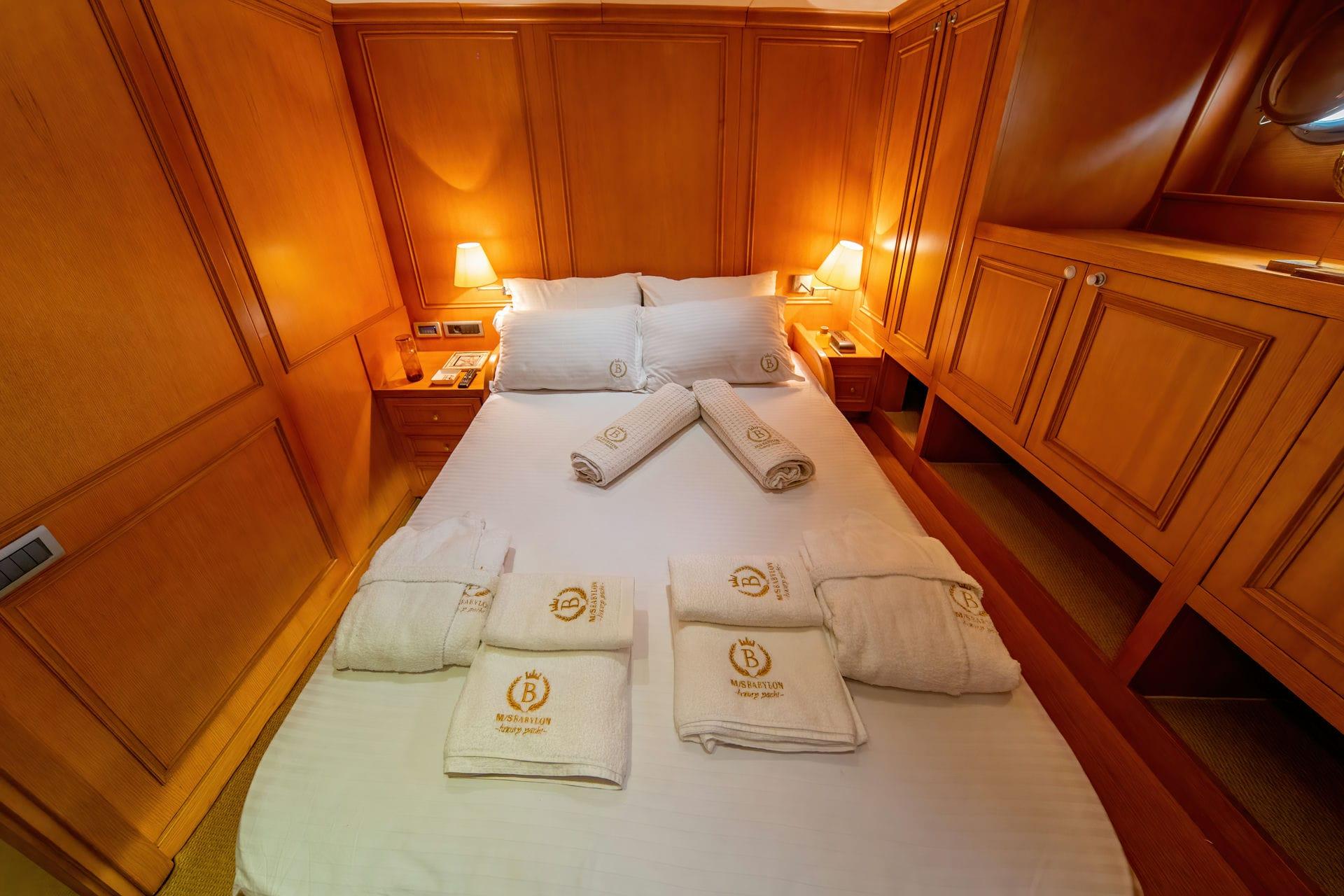 yacht guest cabin with double bed, wooden paneling, bedside lamps and branded towels