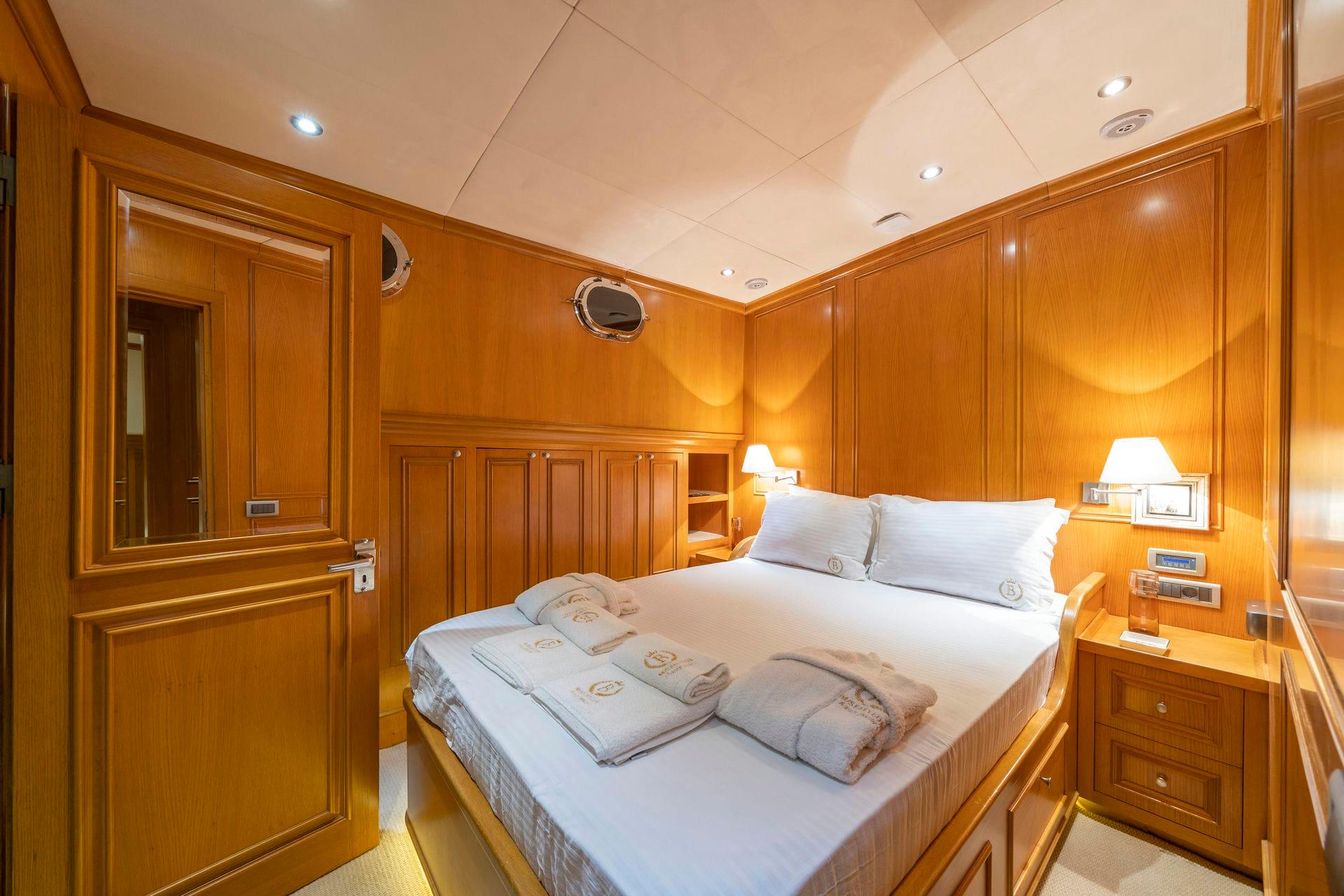 yacht guest cabin featuring double bed with white linens, warm wood paneling, two portholes, and built-in storage
