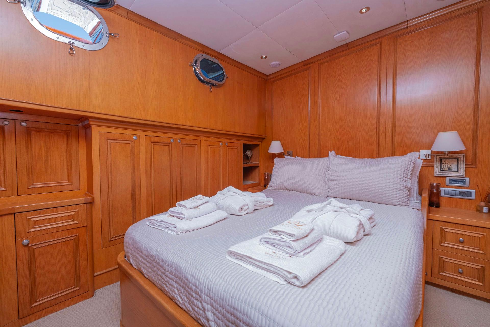 yacht cabin interior featuring double bed with white linens and extensive teak wood cabinetry