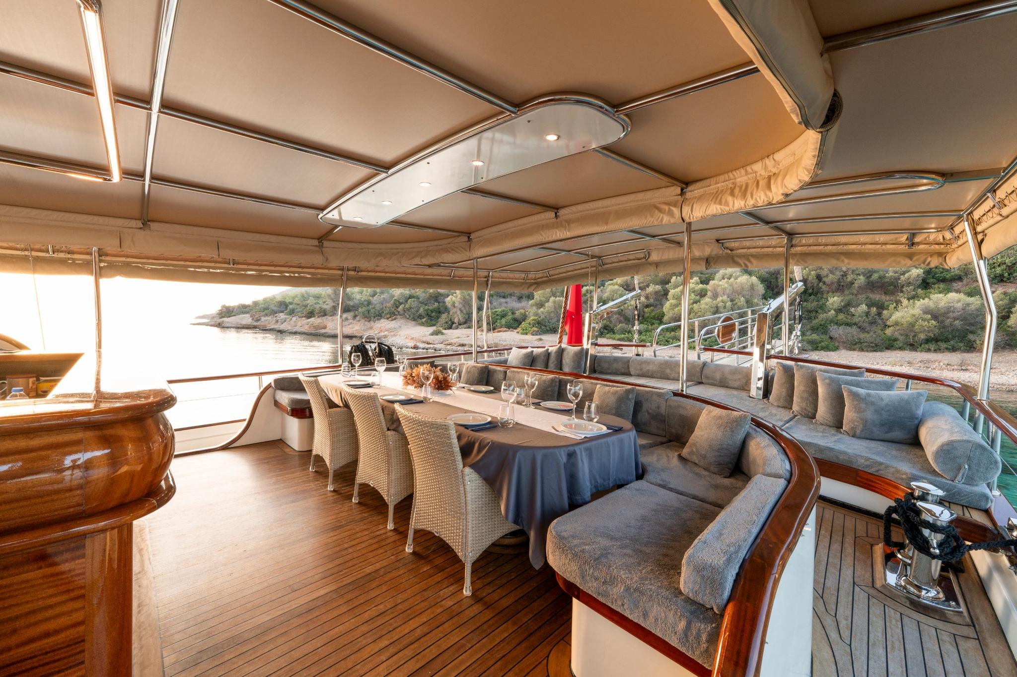 covered aft deck with curved banquette seating, dining table and wicker chairs on teak flooring