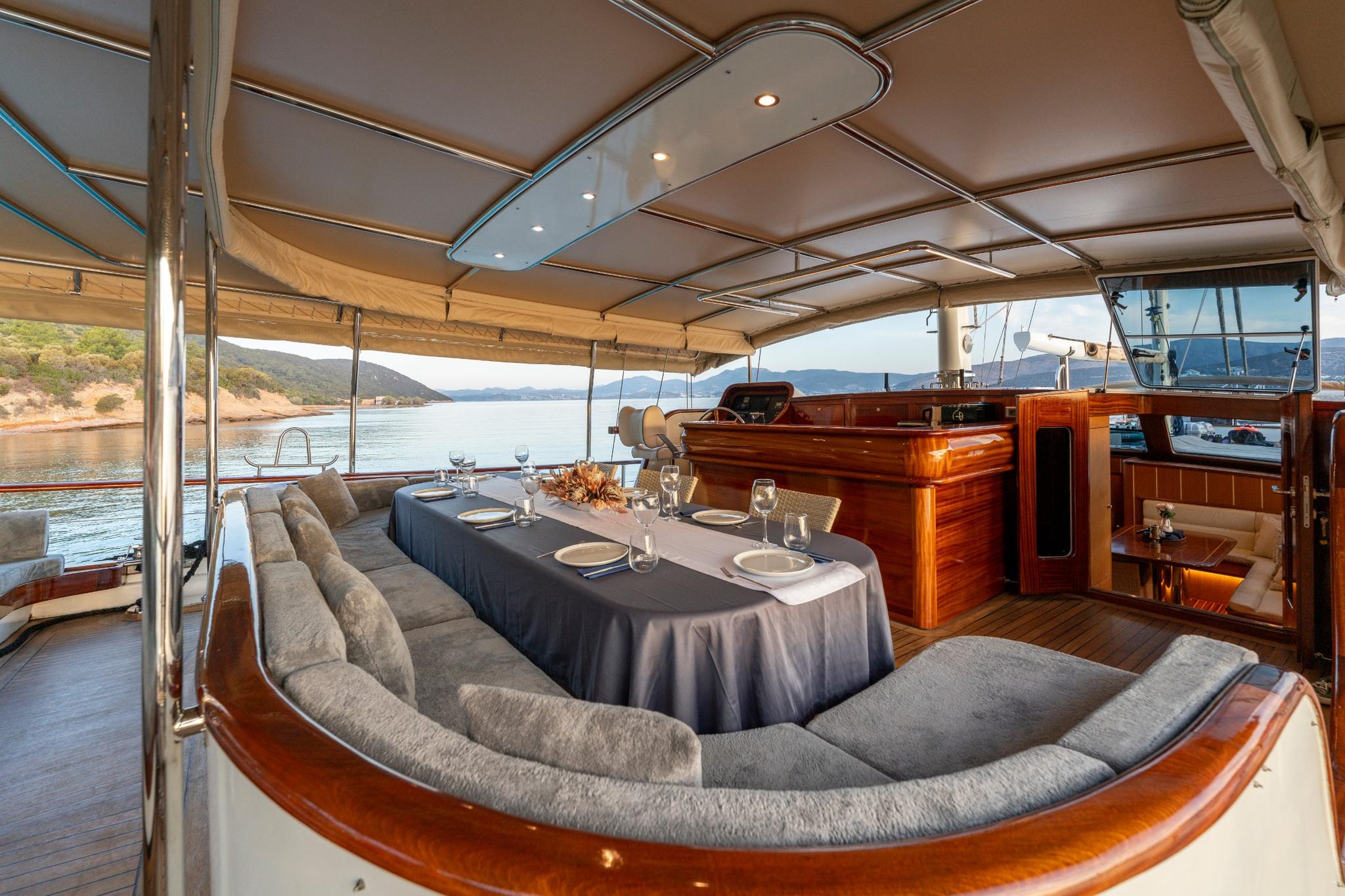 gulet aft deck with formal dining table, curved seating, and coastal anchorage view