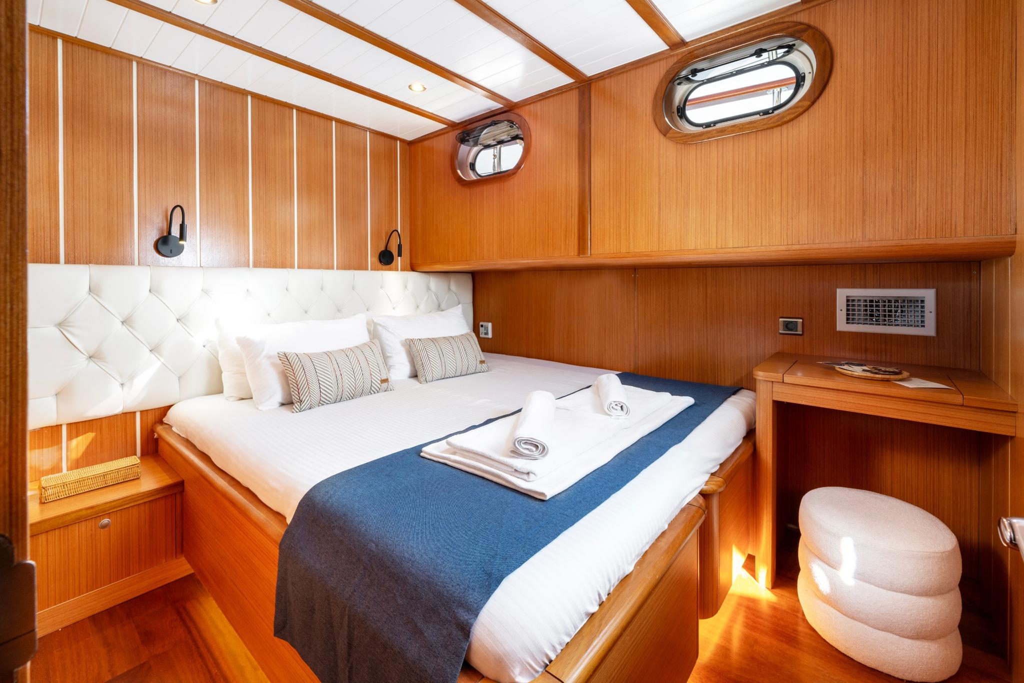 yacht cabin interior with double bed, tufted white headboard, wood paneling and portholes