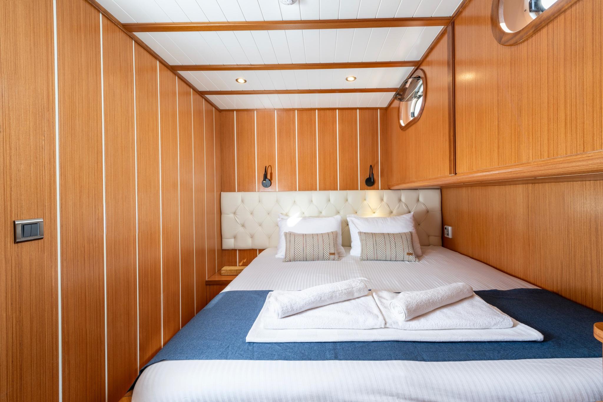 yacht guest cabin featuring double bed with white tufted leather headboard and warm wood paneling