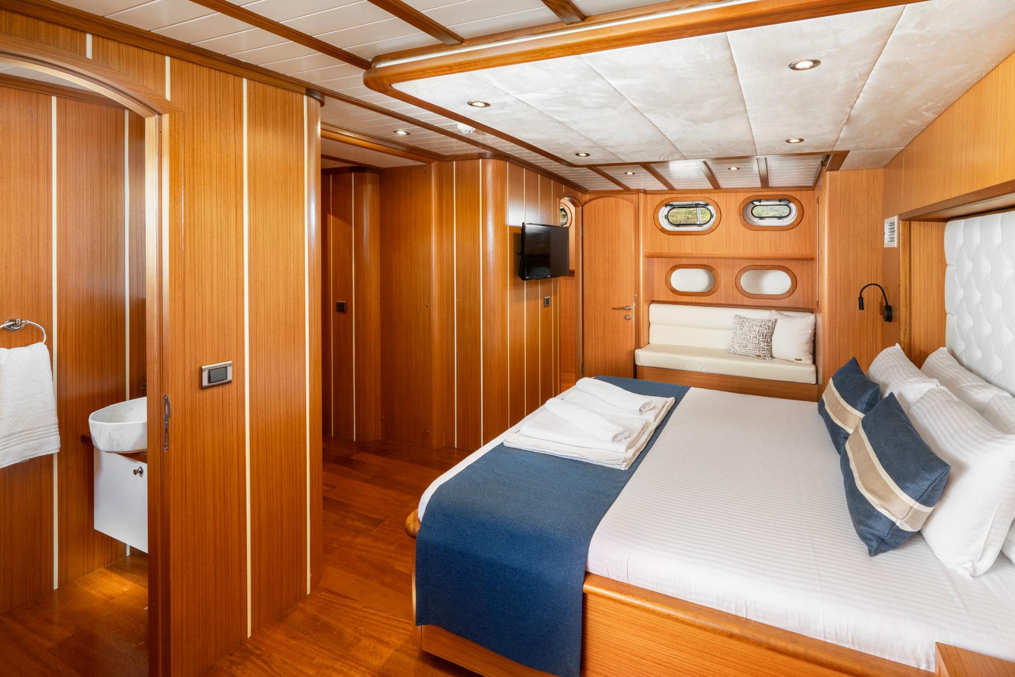 yacht cabin interior with double bed, blue runner, wood paneling and en-suite bathroom