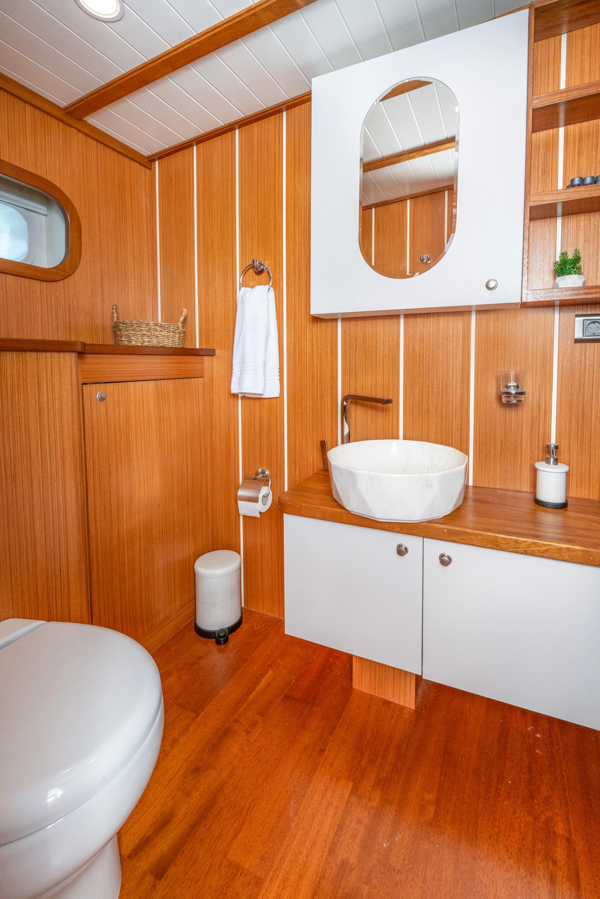 yacht bathroom interior with white vessel sink, teak wood paneling and white ceiling