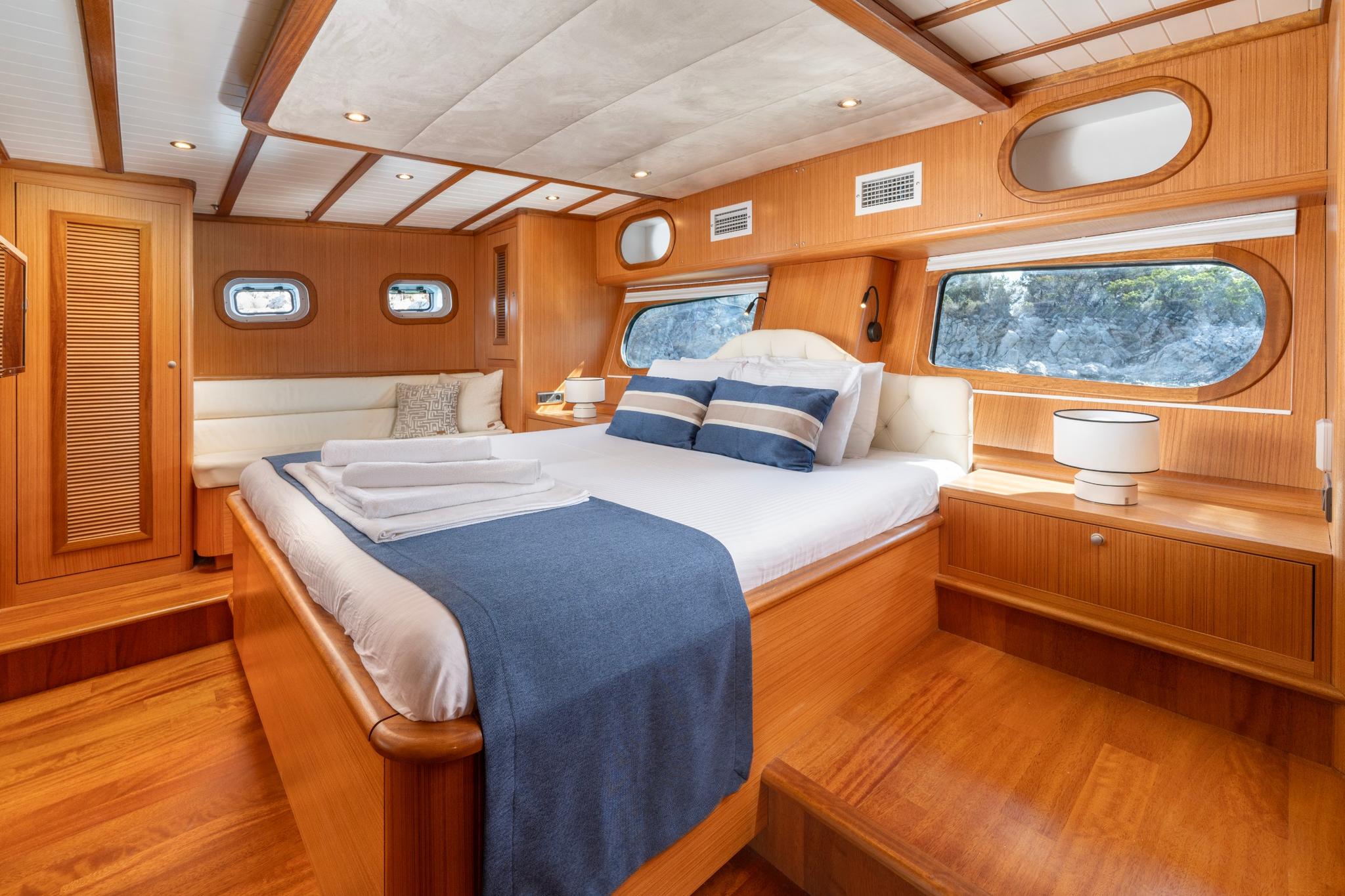 yacht cabin interior featuring double bed with blue runner, wood paneled walls and portholes