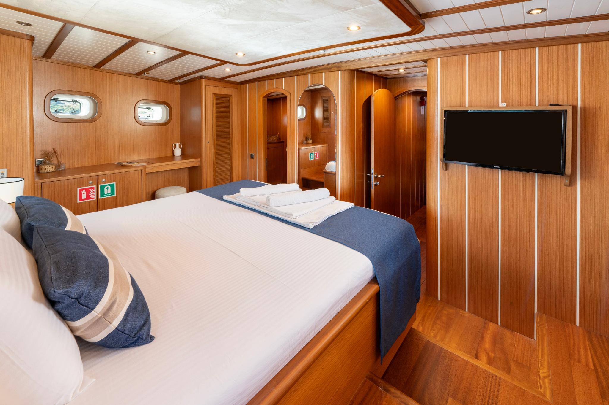 yacht guest cabin with double bed, wood paneling, portholes and en-suite bathroom entrance