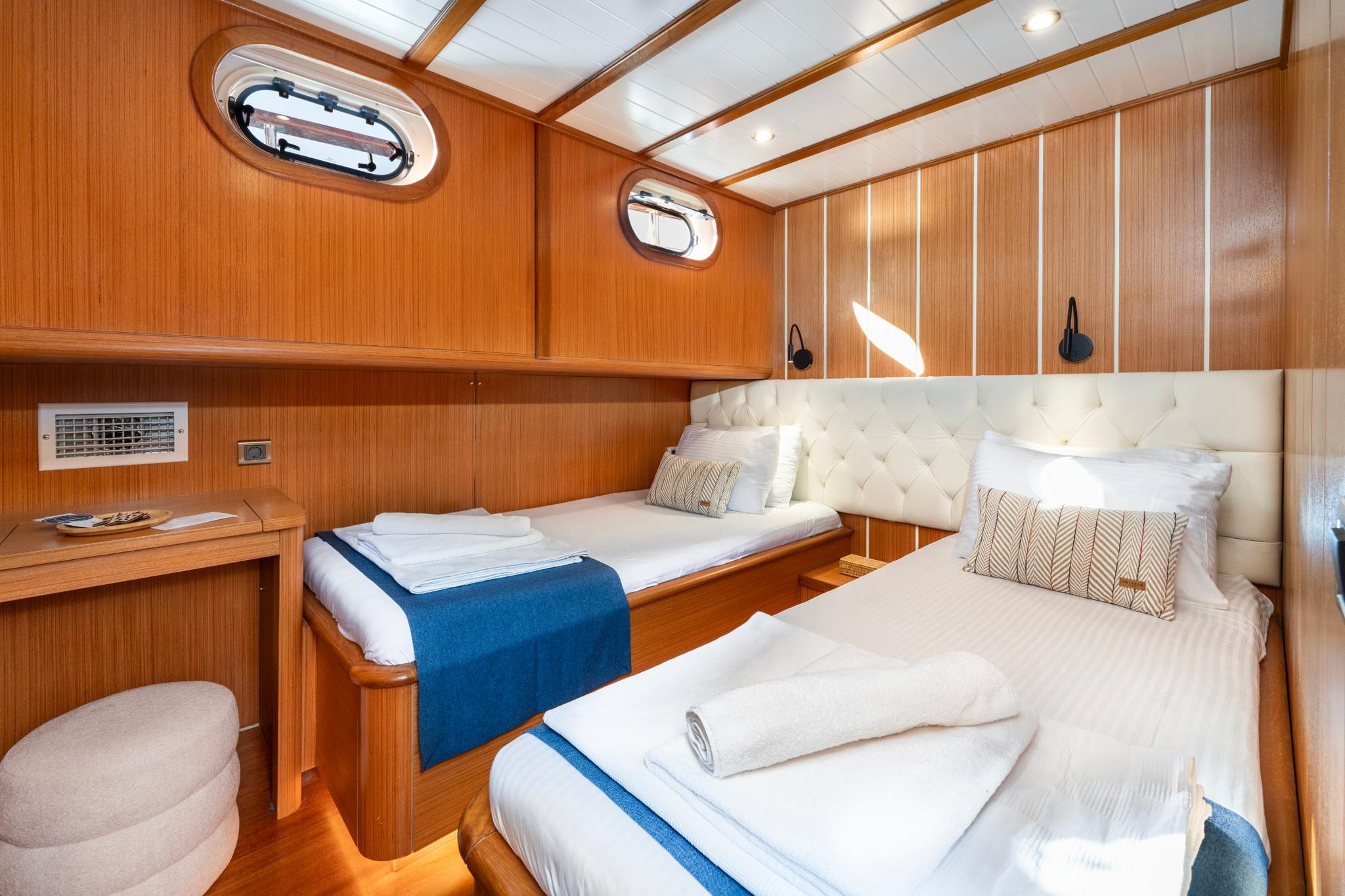guest cabin interior featuring twin beds with white tufted headboard and teak paneling