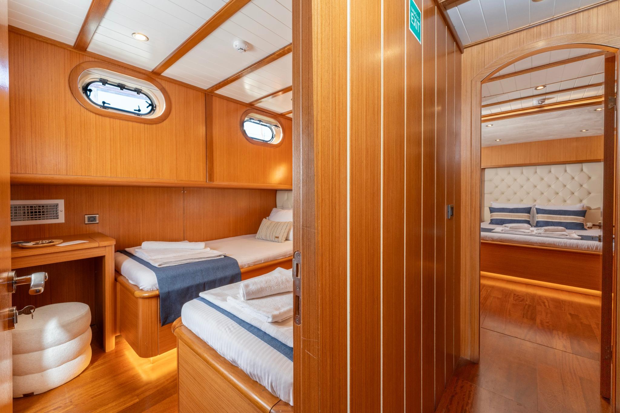 yacht guest cabin interior with single bed, wooden paneling, and round porthole windows