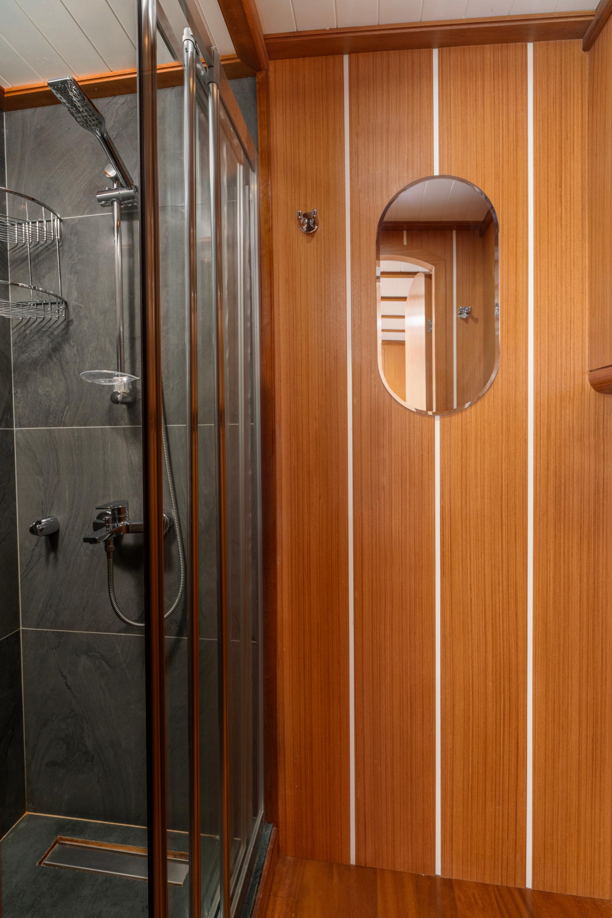 yacht bathroom featuring glass shower enclosure, dark marble walls, and teak wood paneling with oval mirror