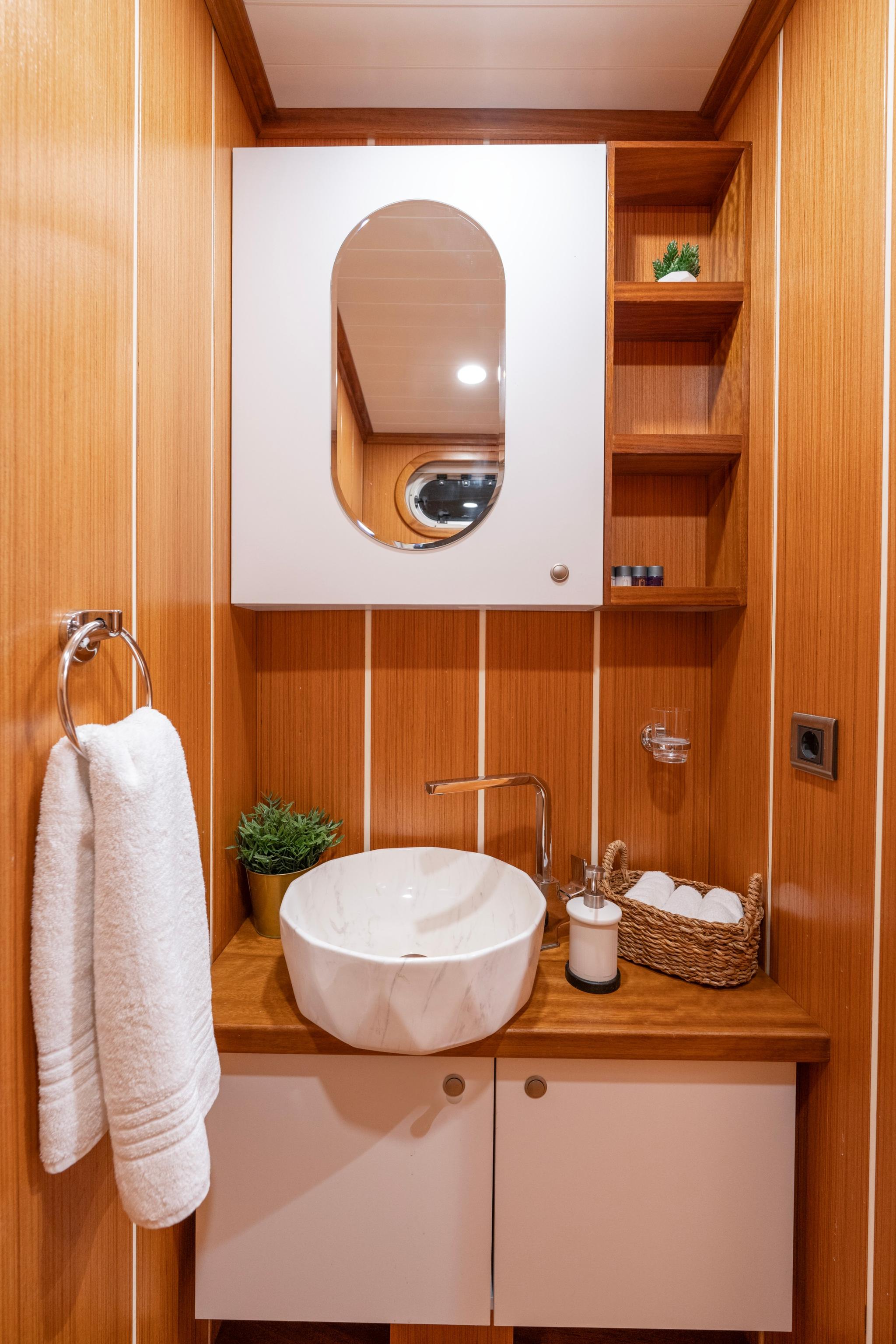 Compact yacht bathroom featuring white vessel basin, teak wood paneling and built-in storage