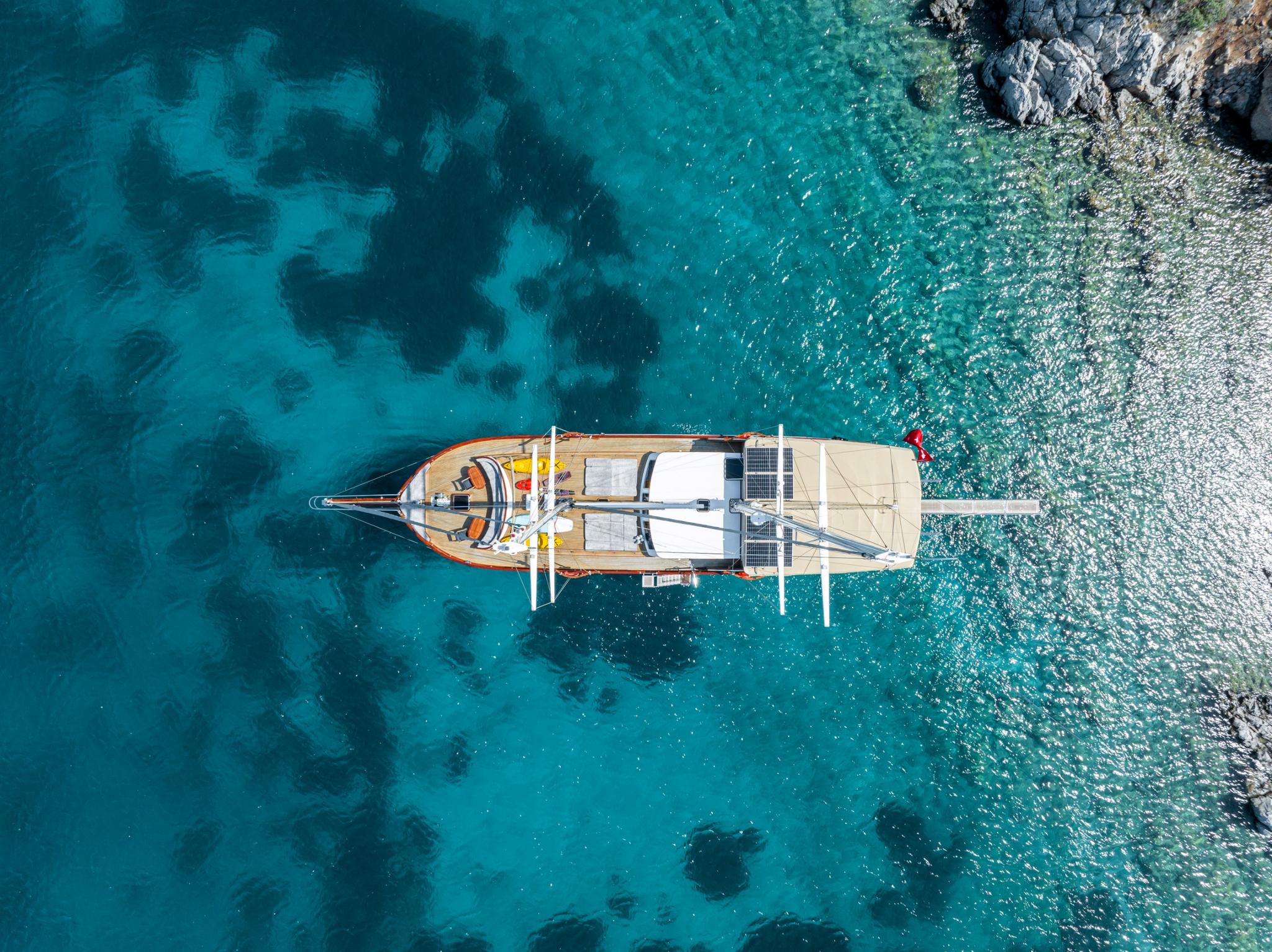 Drone shot of traditional wooden gulet yacht anchored in crystal clear turquoise Mediterranean waters near rocky coastline