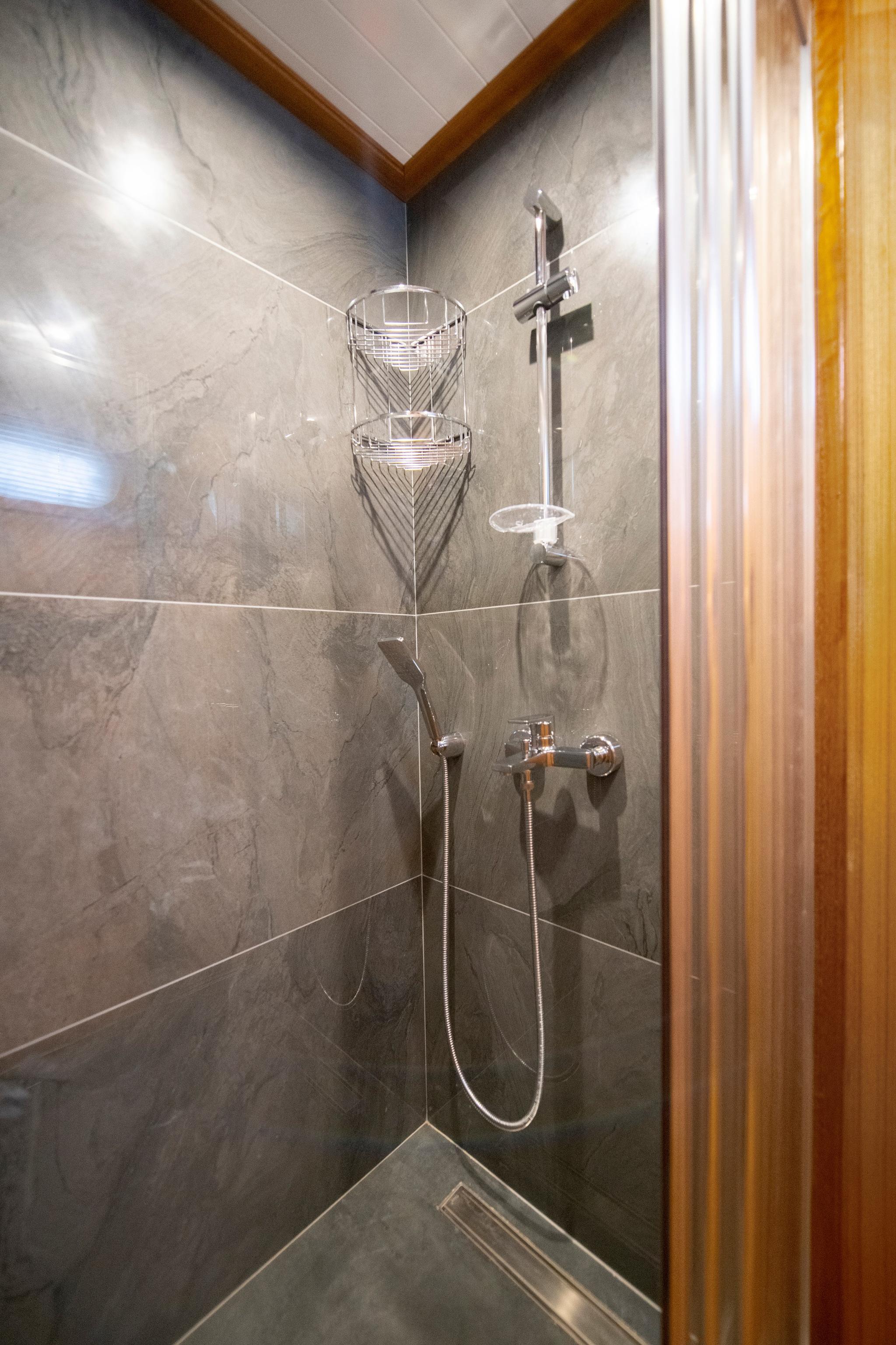 yacht shower compartment with grey marble walls, chrome fixtures and storage caddy