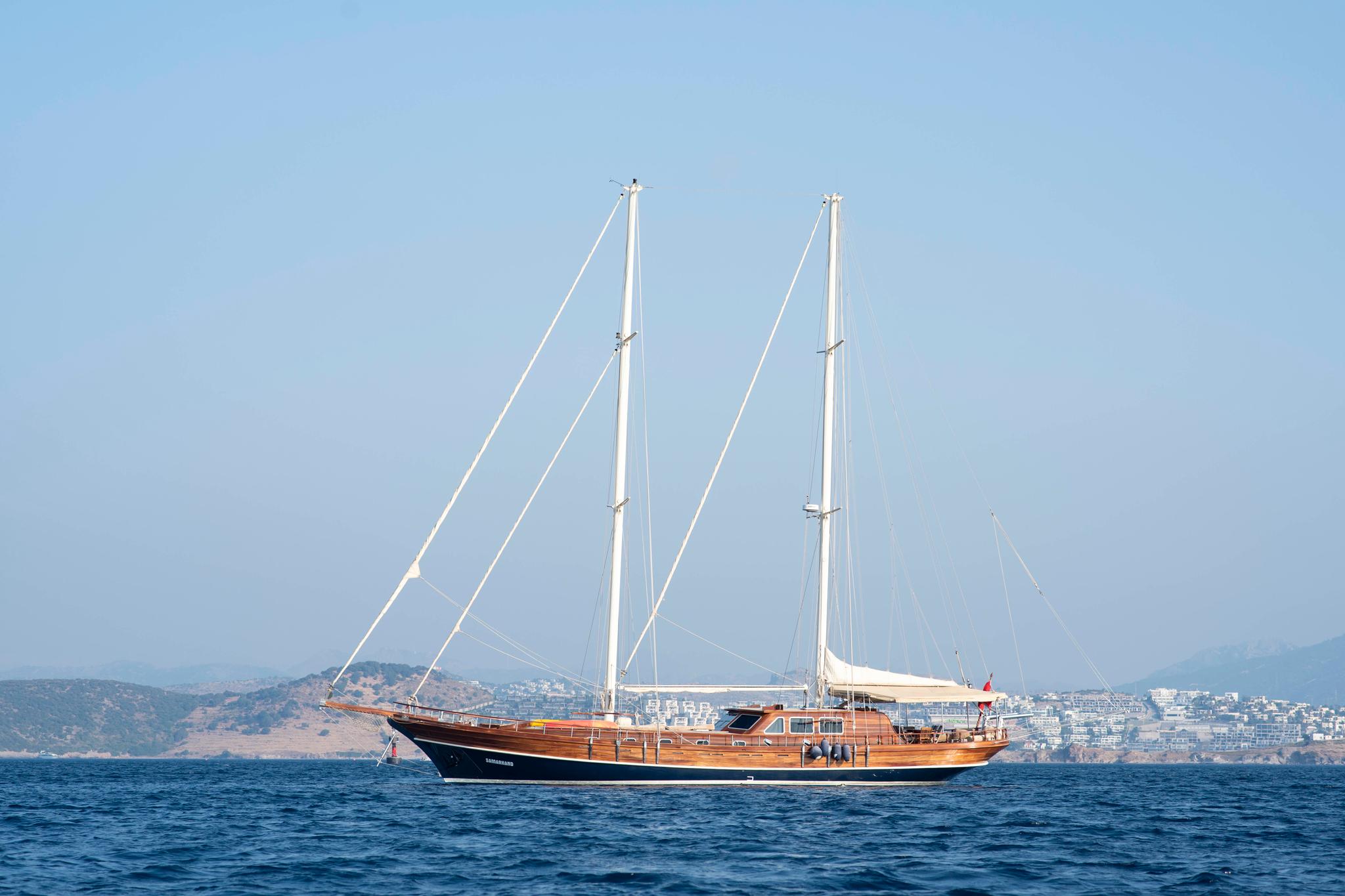wooden gulet yacht with two masts anchored in blue Mediterranean waters near coastal town