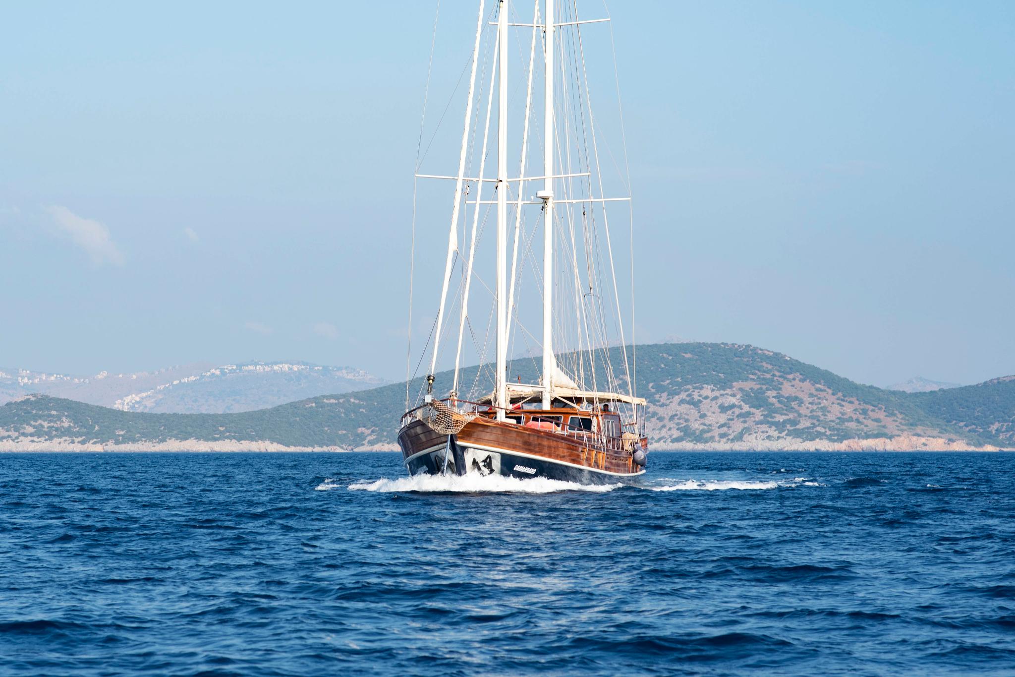wooden gulet yacht under sail with Mediterranean coastline in background