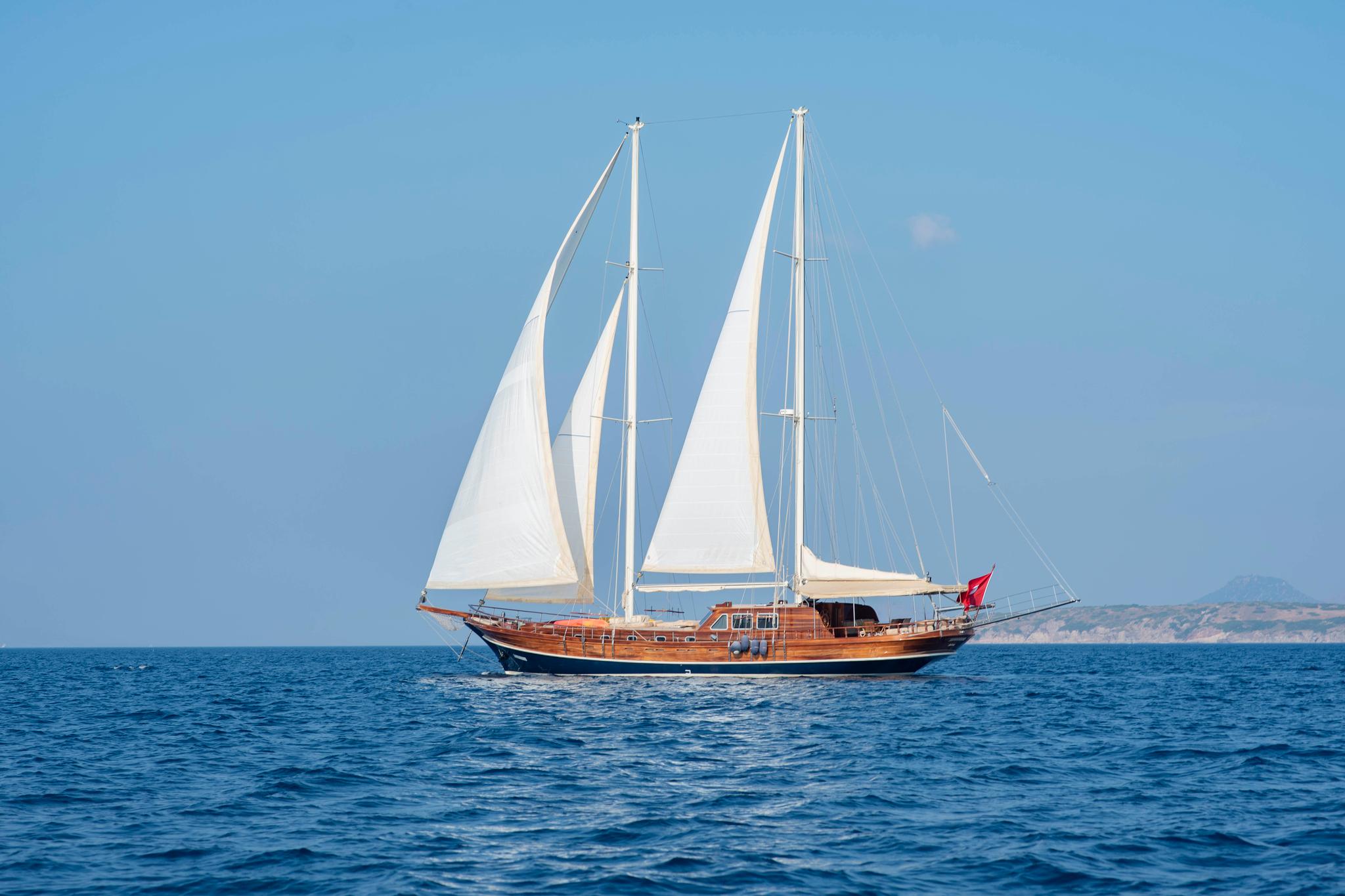 wooden gulet yacht with white sails deployed sailing on calm blue Mediterranean waters