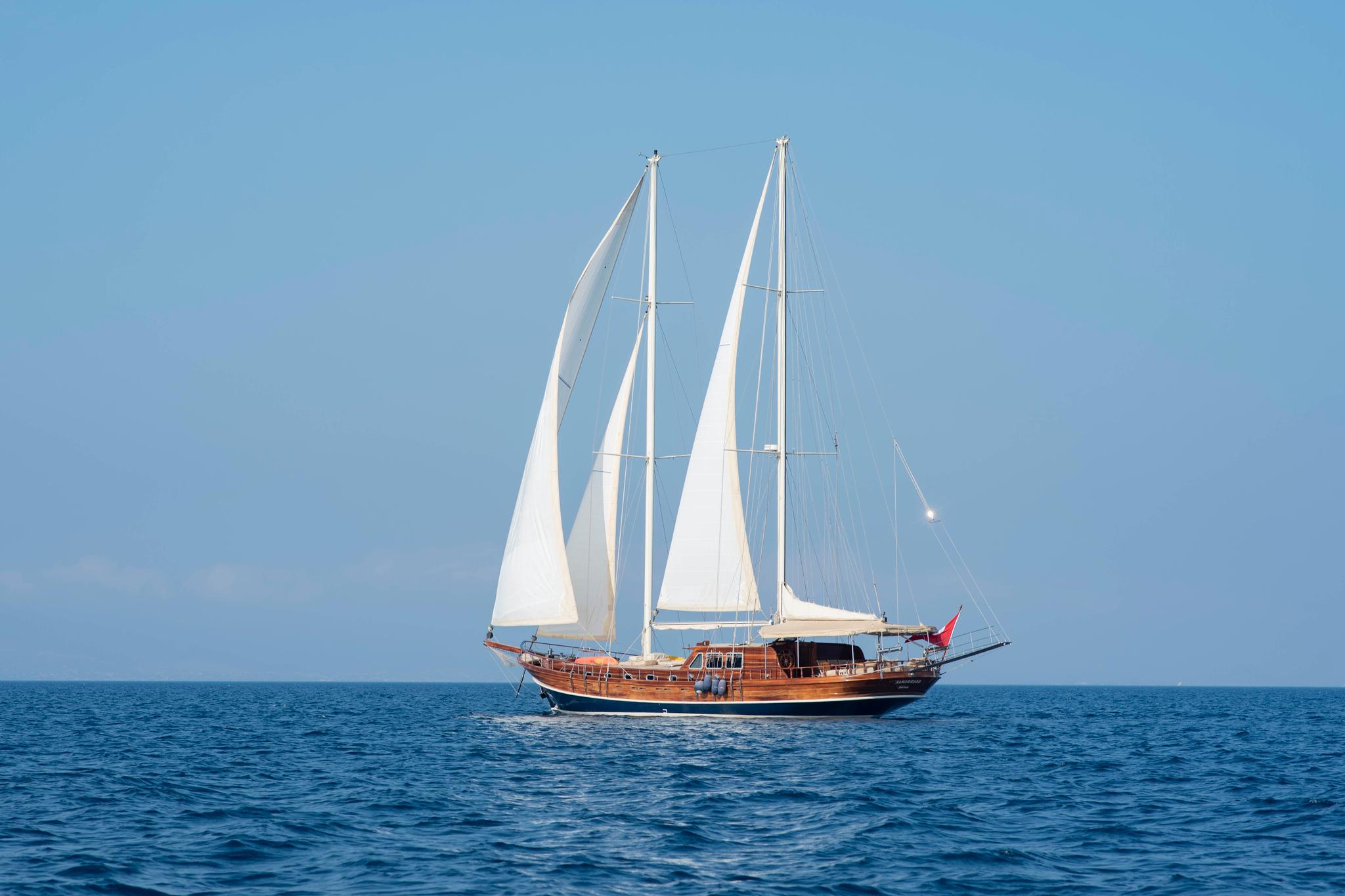 wooden gulet yacht sailing on blue waters with three white sails raised