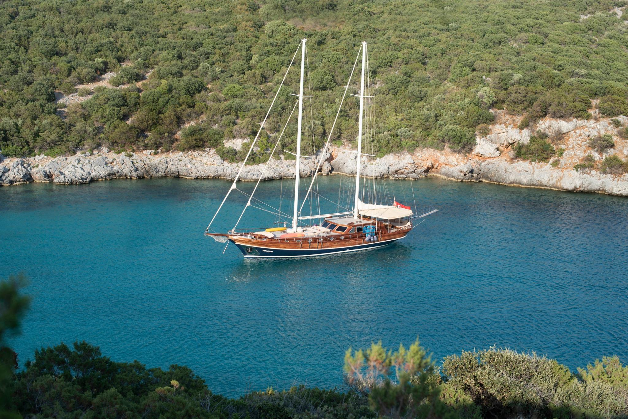 aerial view of wooden gulet yacht anchored in secluded turquoise cove surrounded by rocky coastline