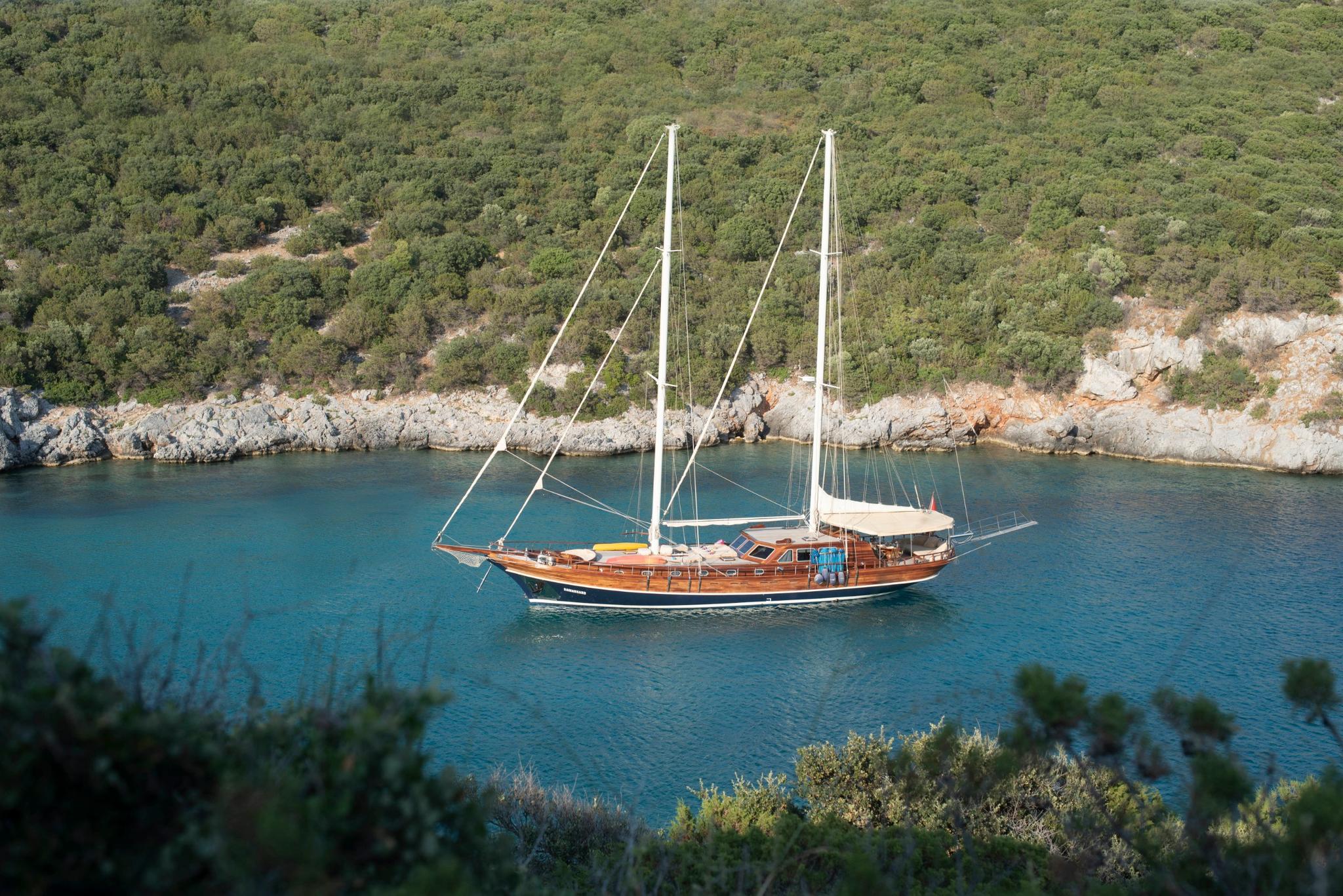 Traditional wooden gulet with two masts anchored in turquoise bay surrounded by forested coastline