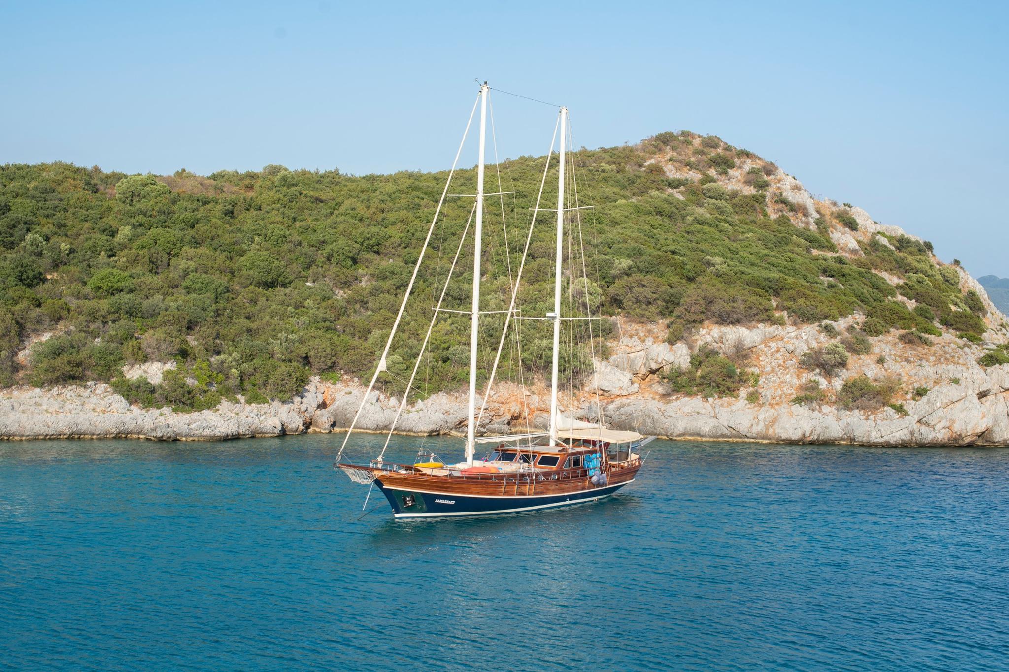 traditional wooden gulet yacht anchored in crystal clear turquoise waters near Mediterranean rocky coastline