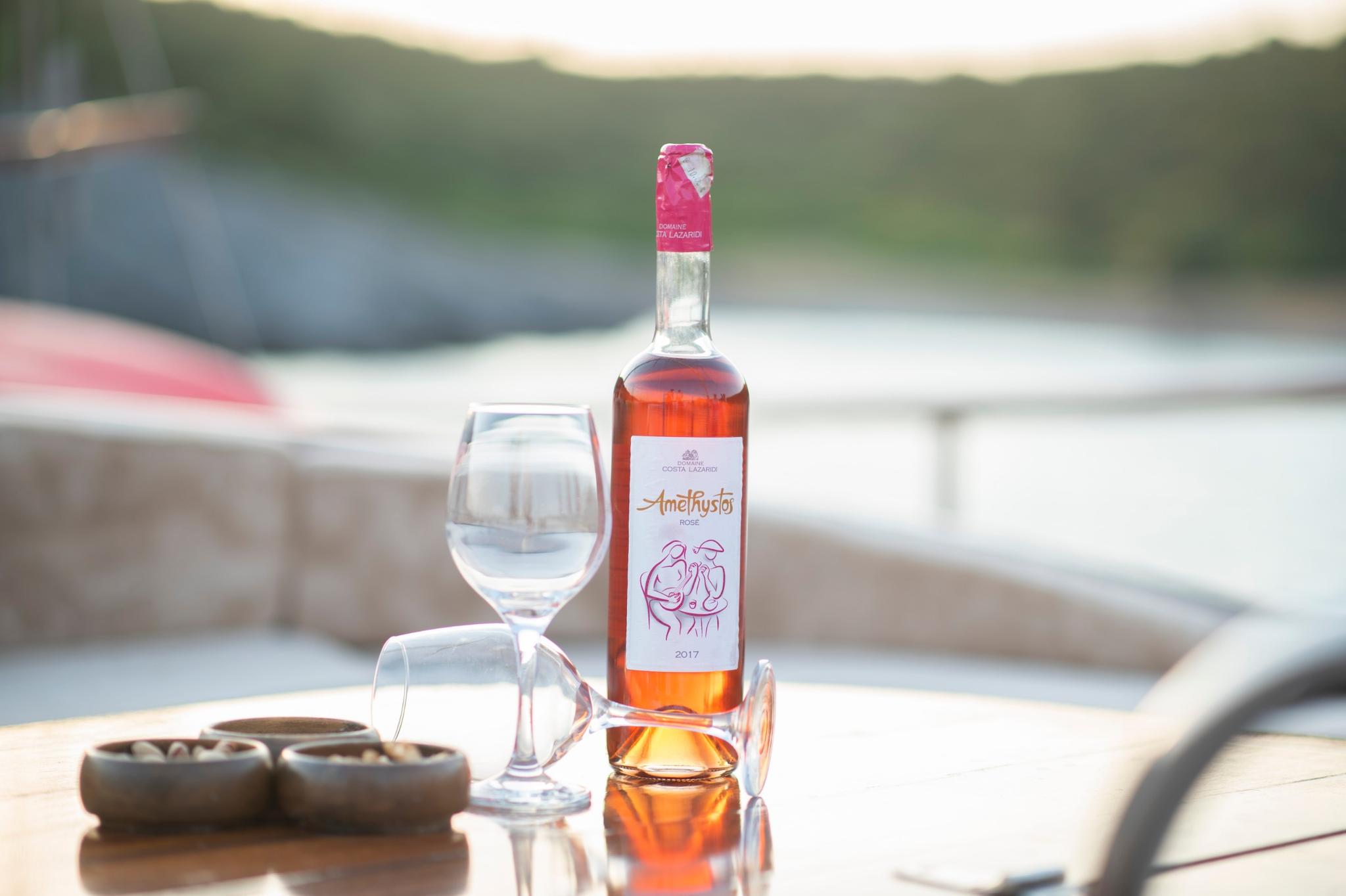 Amethystos rosé wine bottle with glasses on yacht deck table with blurred marina background