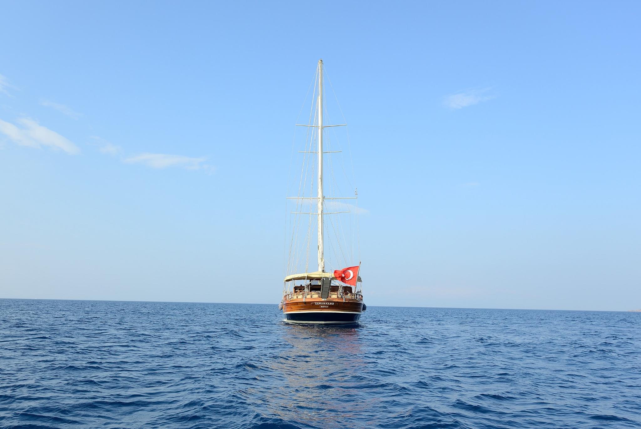wooden gulet yacht with single mast and Turkish flag anchored in calm blue waters