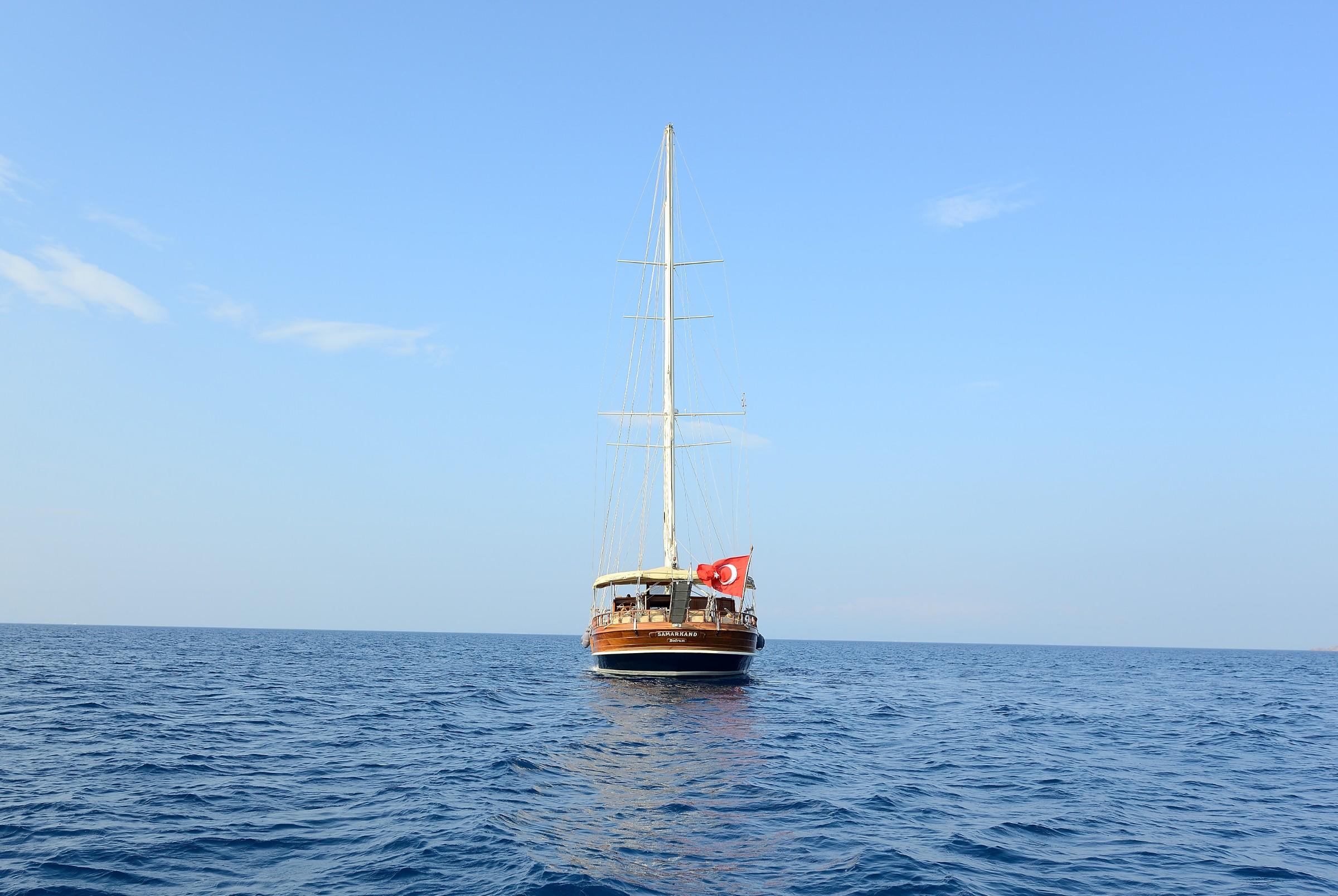 wooden gulet yacht with single mast and Turkish flag anchored in calm blue waters
