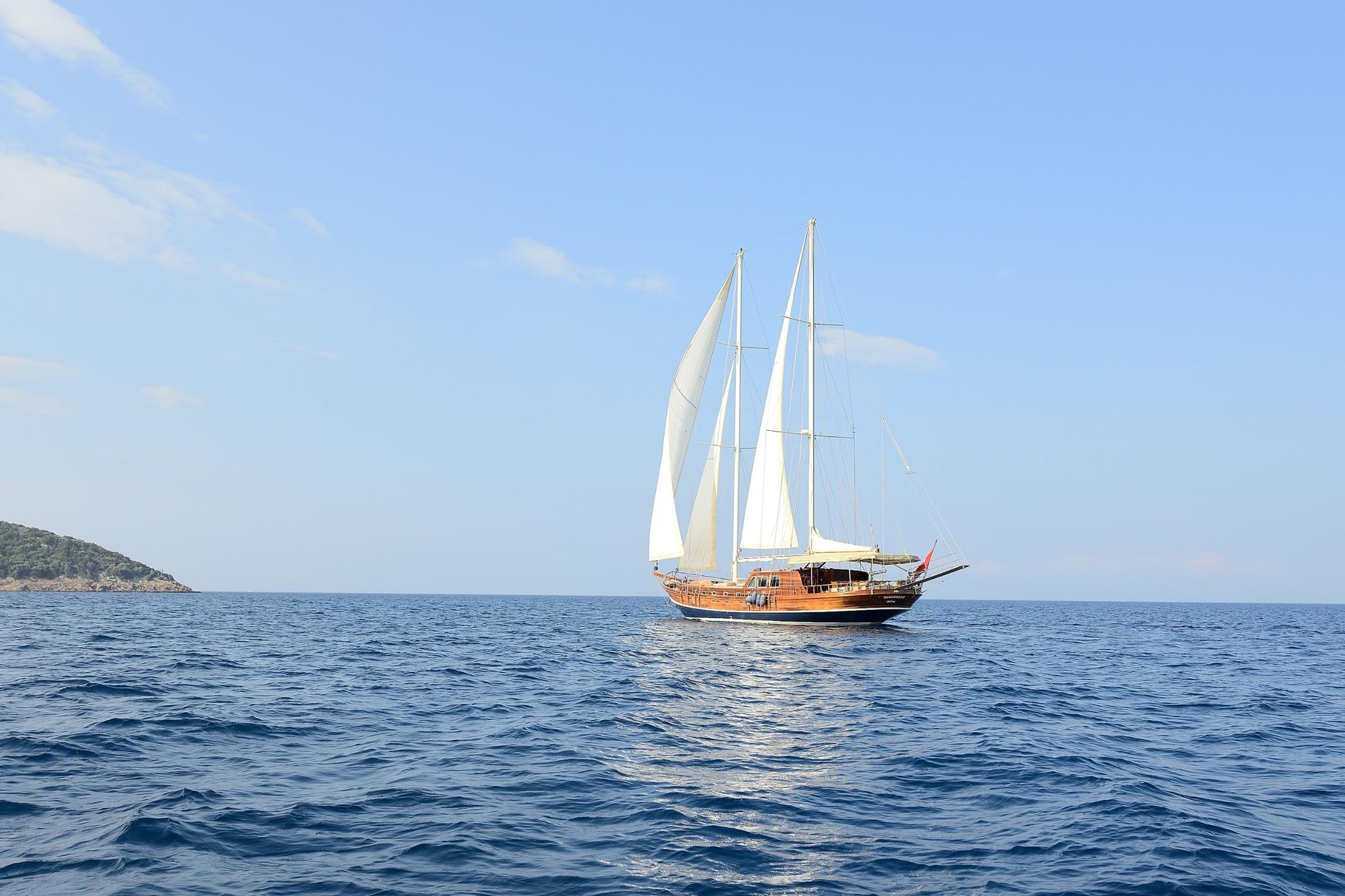 Traditional wooden gulet under sail with two white sails on blue Mediterranean waters