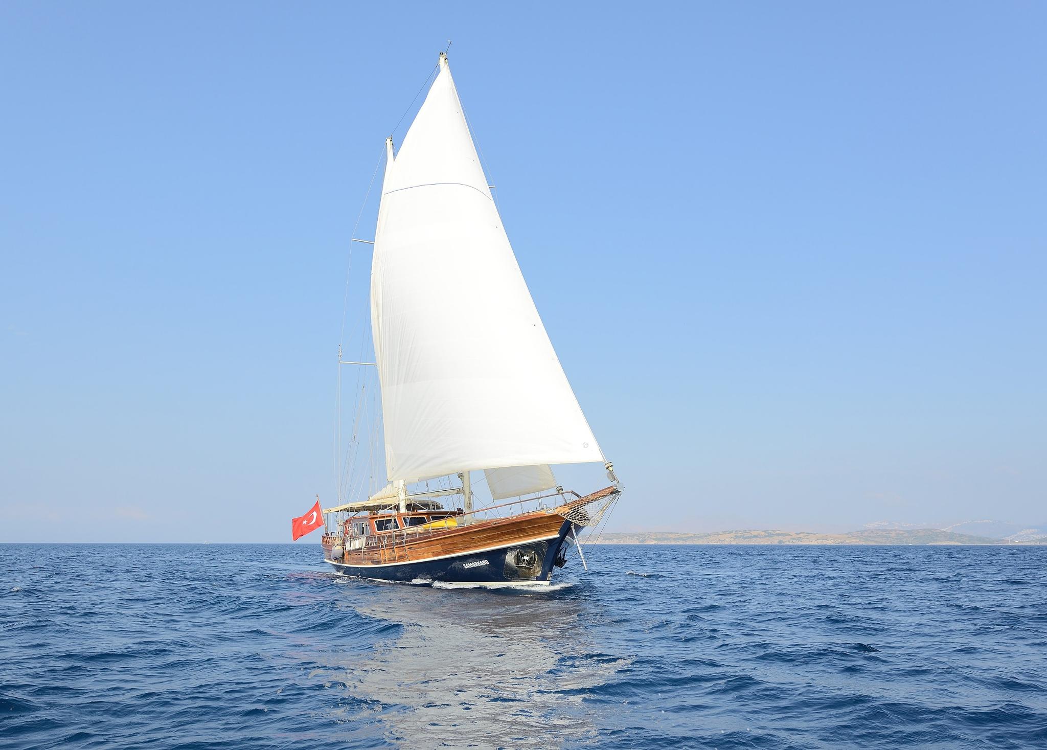 Traditional wooden gulet with white mainsail sailing on blue Mediterranean waters with Turkish flag