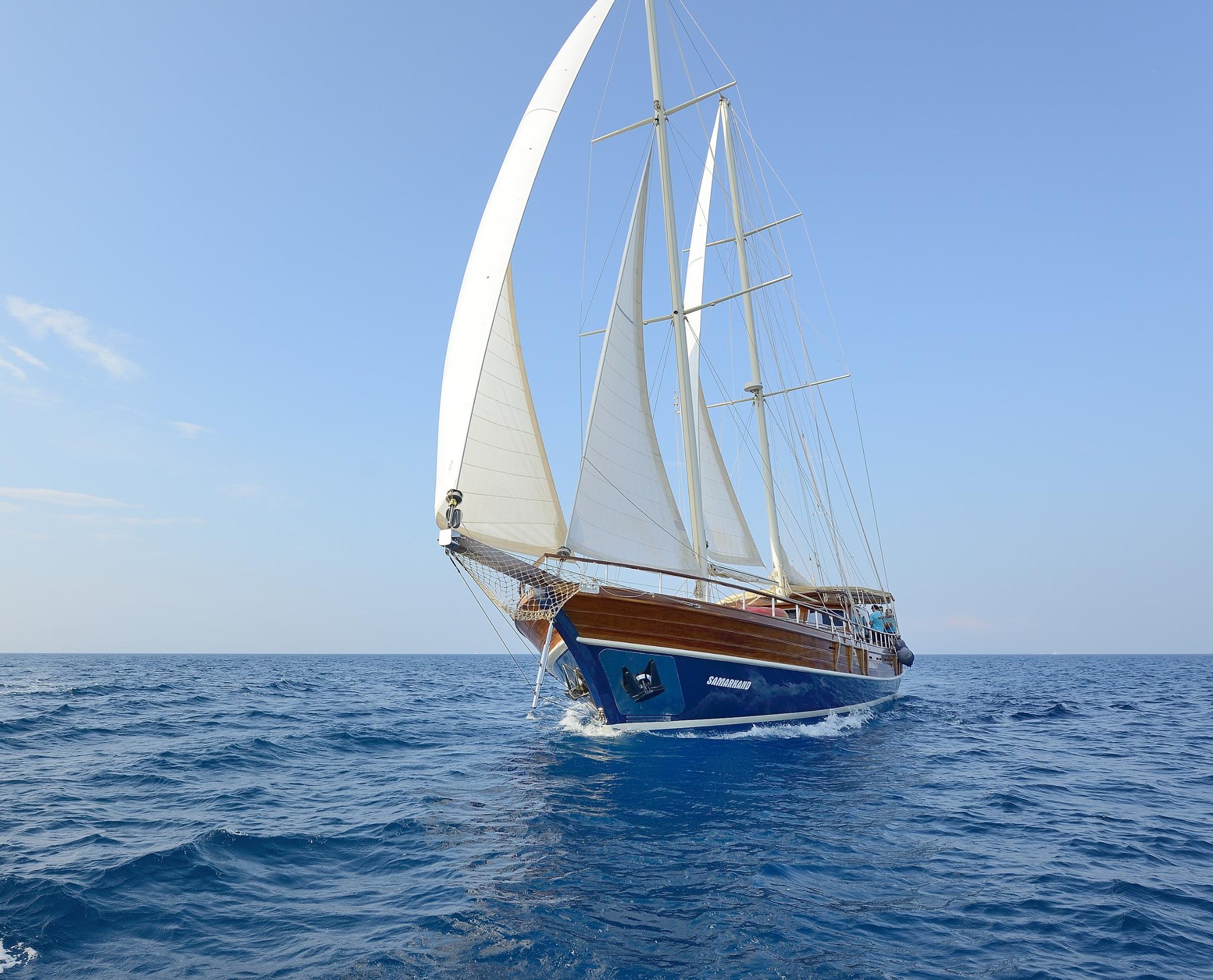 traditional wooden gulet with blue hull and white sails sailing on open blue water