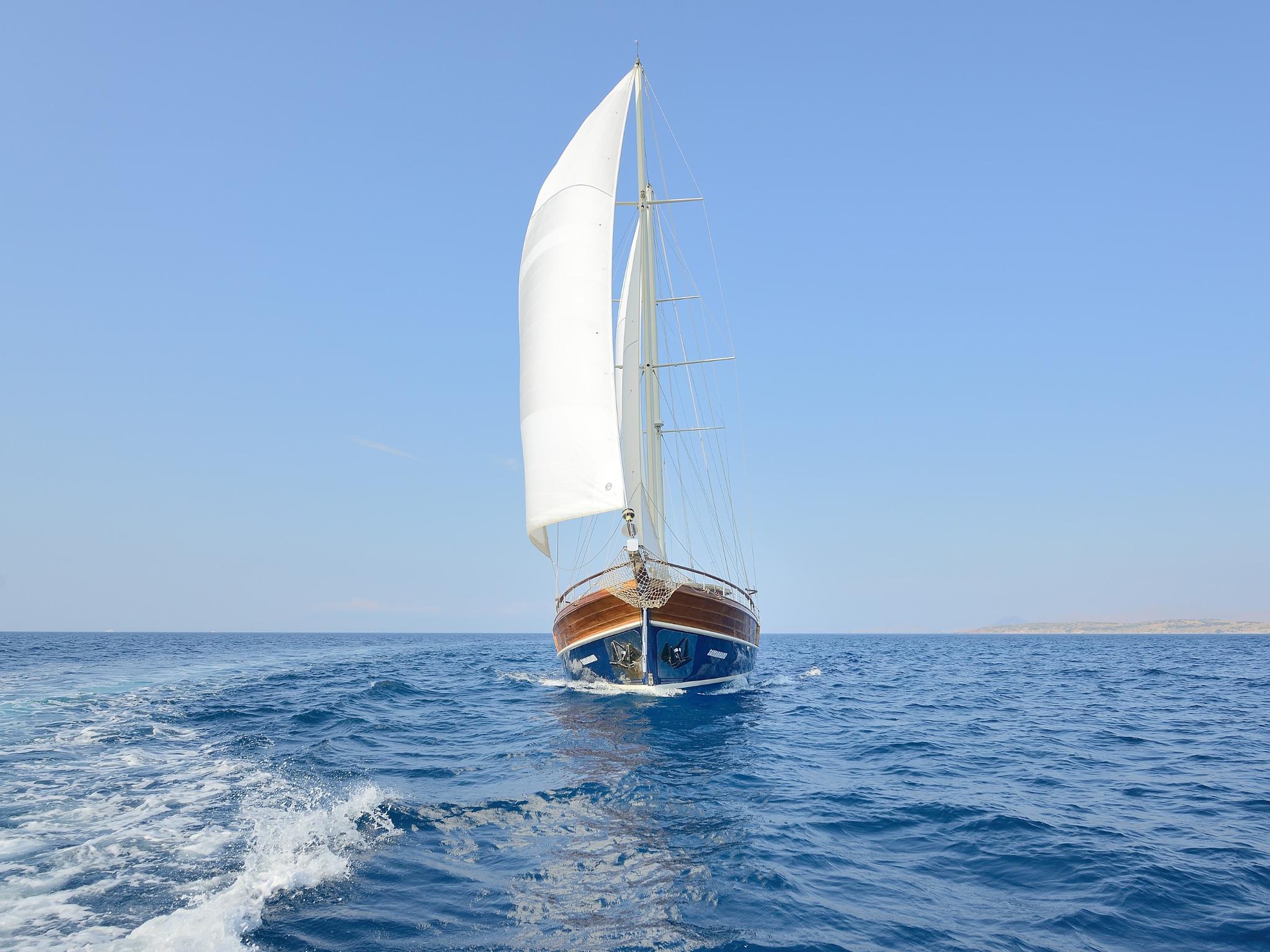 Traditional wooden gulet with white sails deployed sailing on calm blue Mediterranean waters