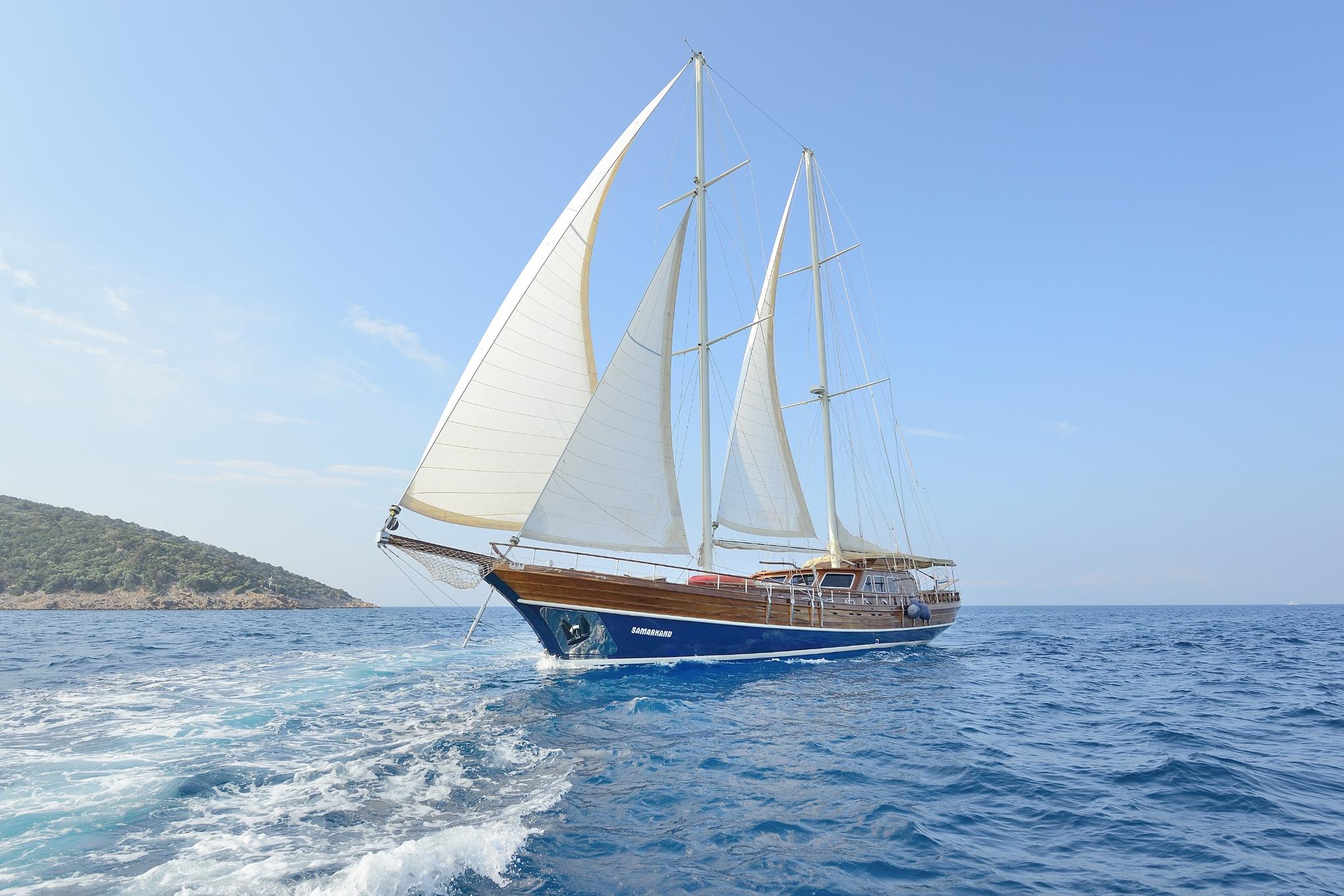 Traditional wooden gulet with three white sails sailing in blue Mediterranean waters