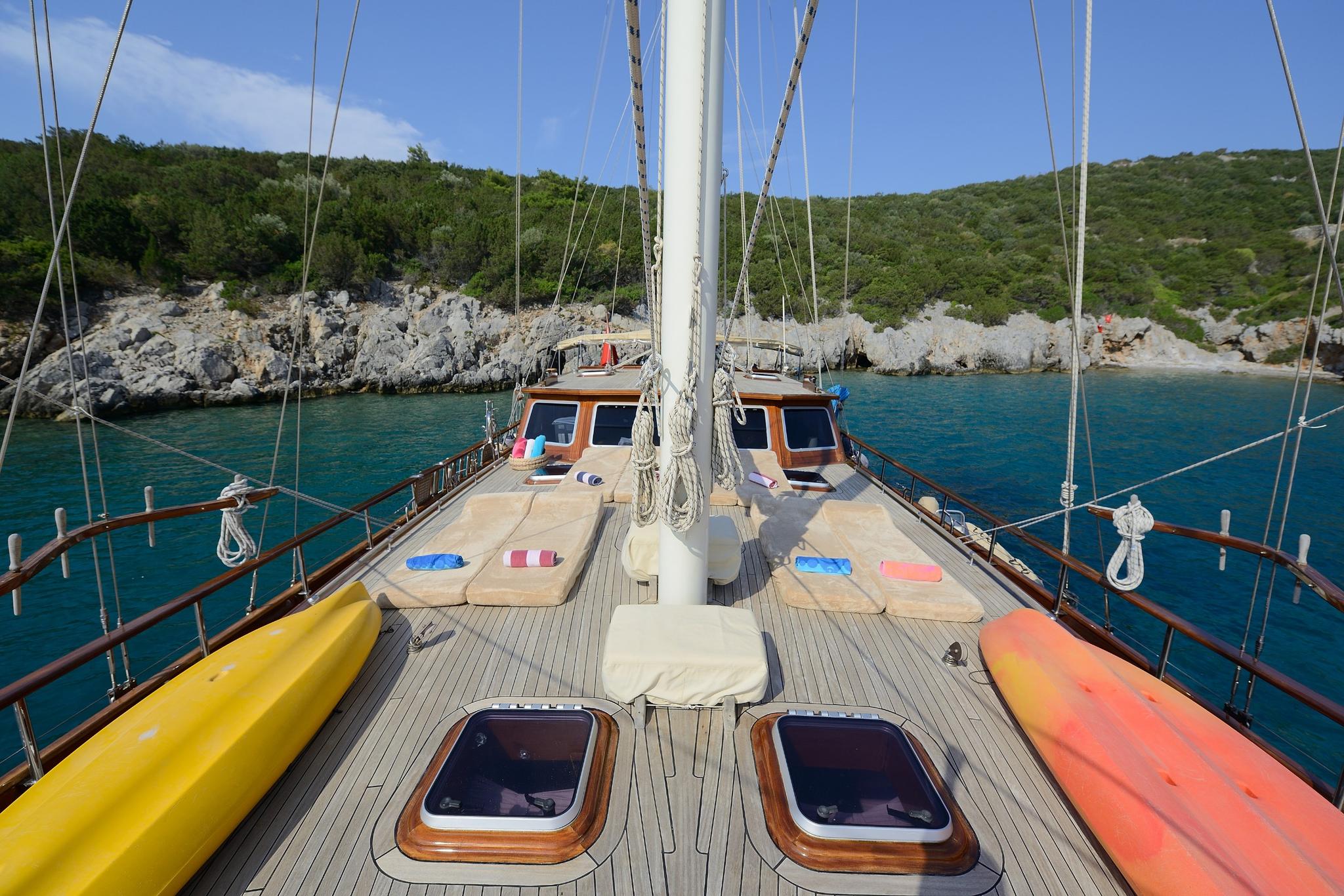 gulet foredeck with teak decking, white sun cushions, yellow and orange kayaks, central mast and rigging