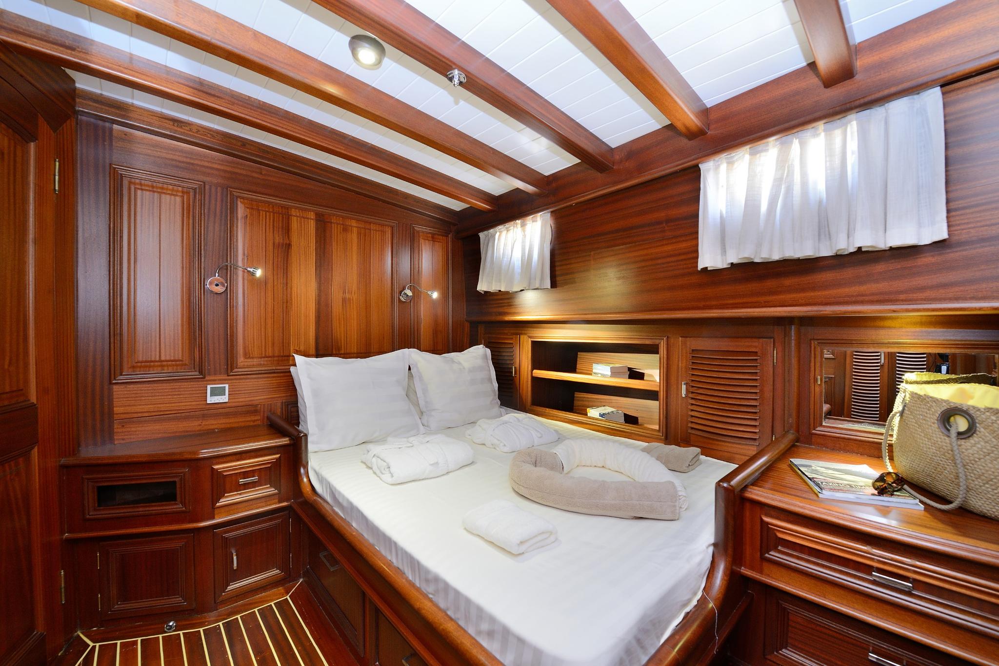 yacht guest cabin featuring double bed with white linens, rich wooden paneling and exposed ceiling beams