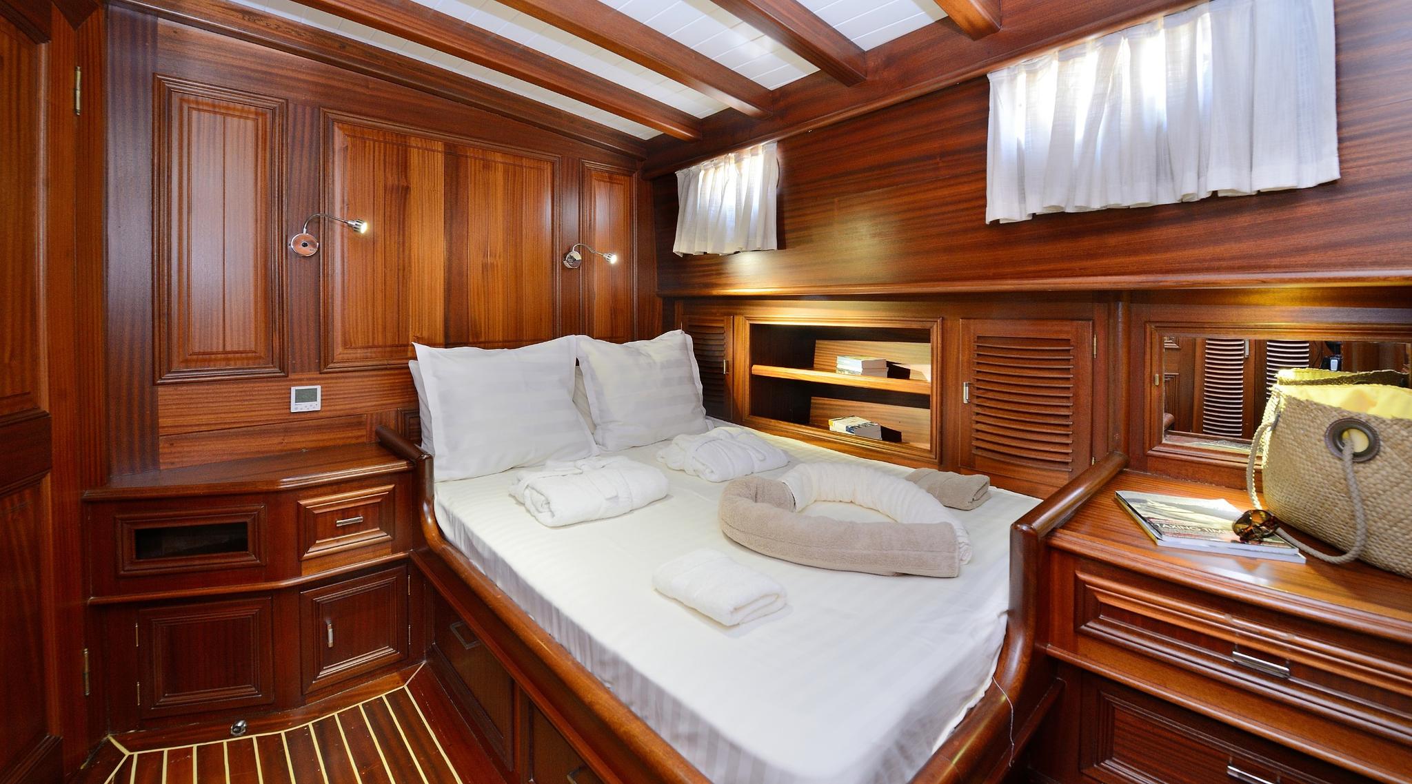yacht guest cabin featuring double bed with white linens and rich wood paneling throughout