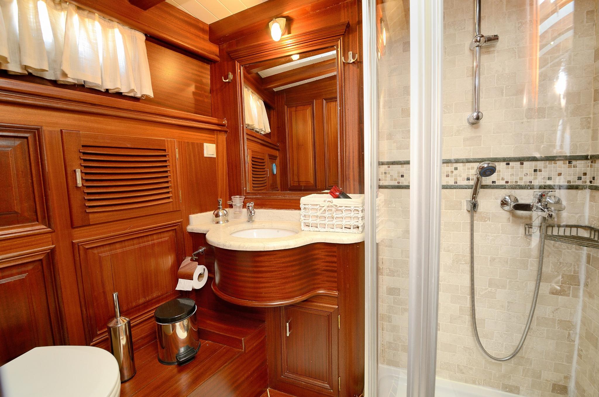 luxury yacht en-suite bathroom featuring marble shower, curved wooden vanity and mirror