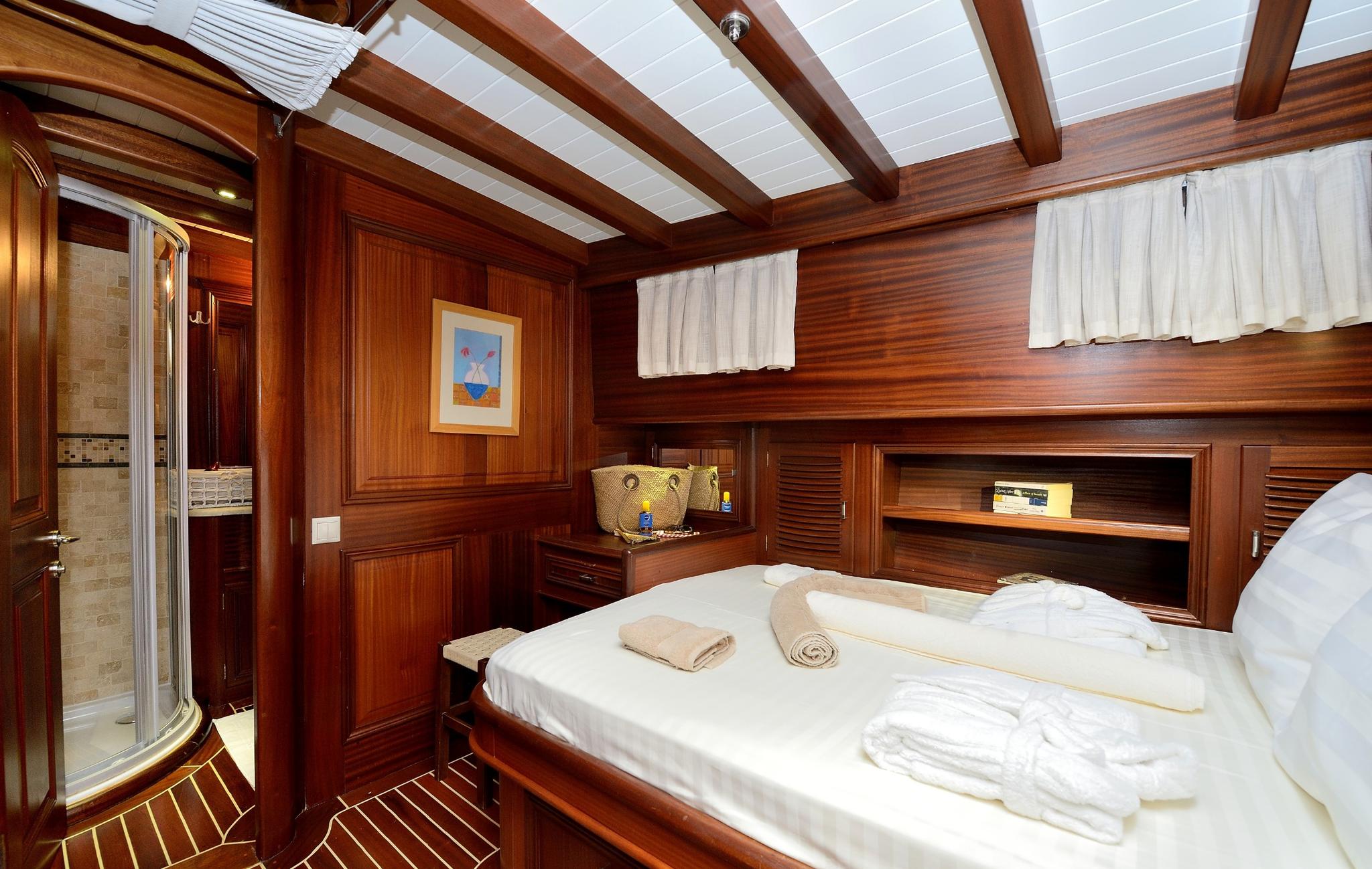 guest cabin featuring double bed with white linens, rich wood paneling, and glass-door en-suite bathroom