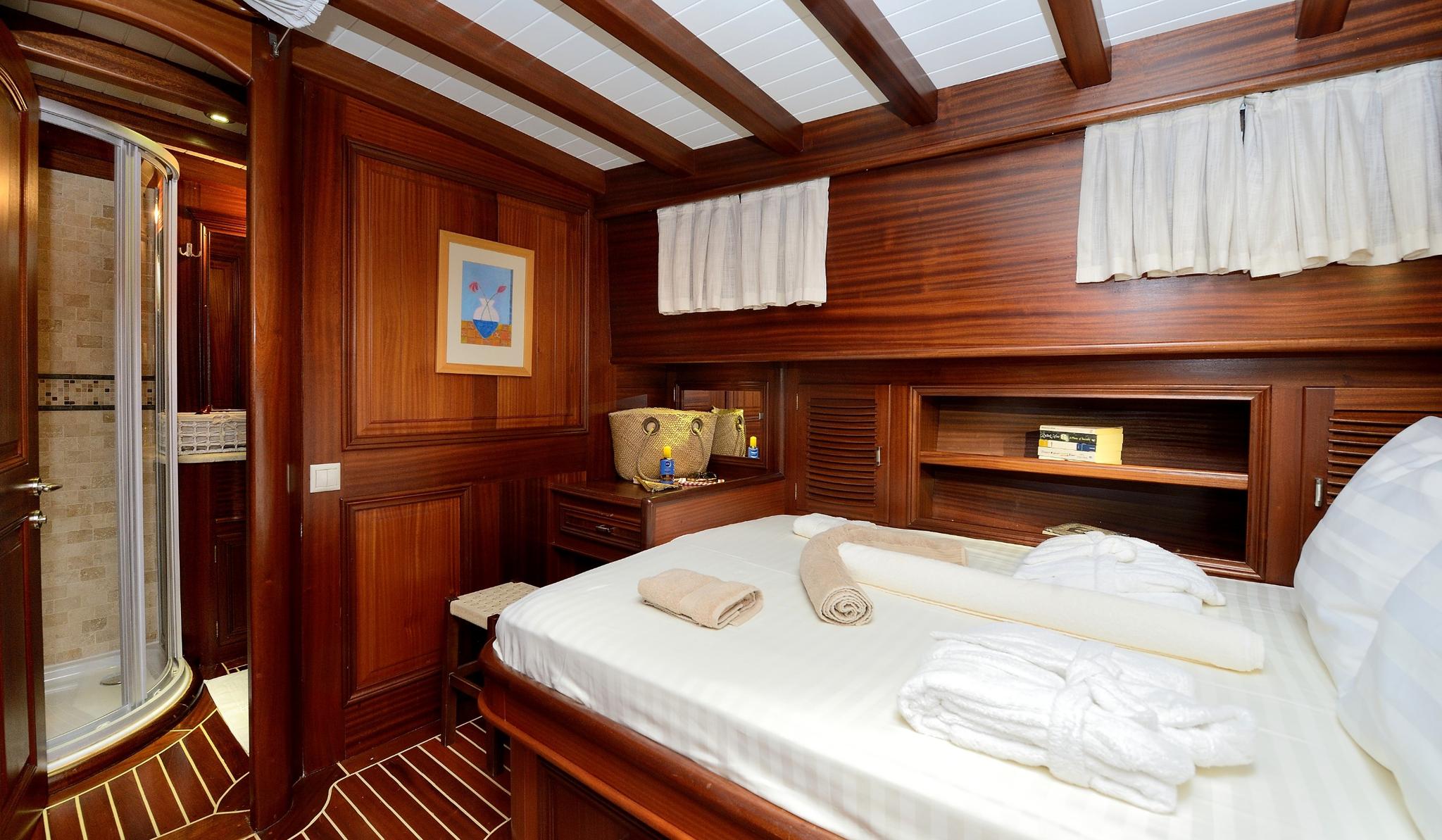 yacht guest cabin featuring double bed with white linens, rich wood paneling, and adjacent en-suite bathroom