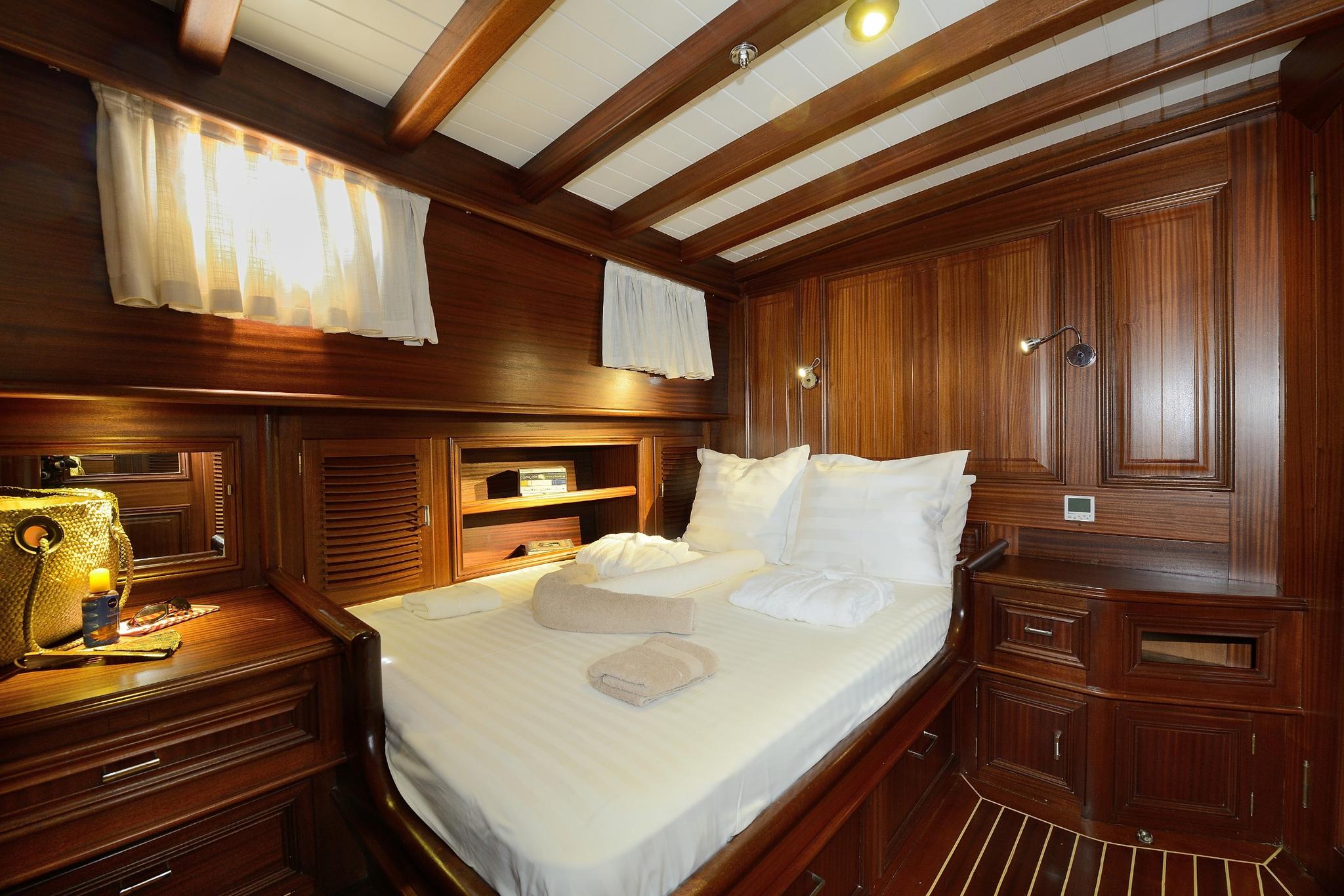 yacht guest cabin featuring double bed with white linens and extensive teak woodwork storage