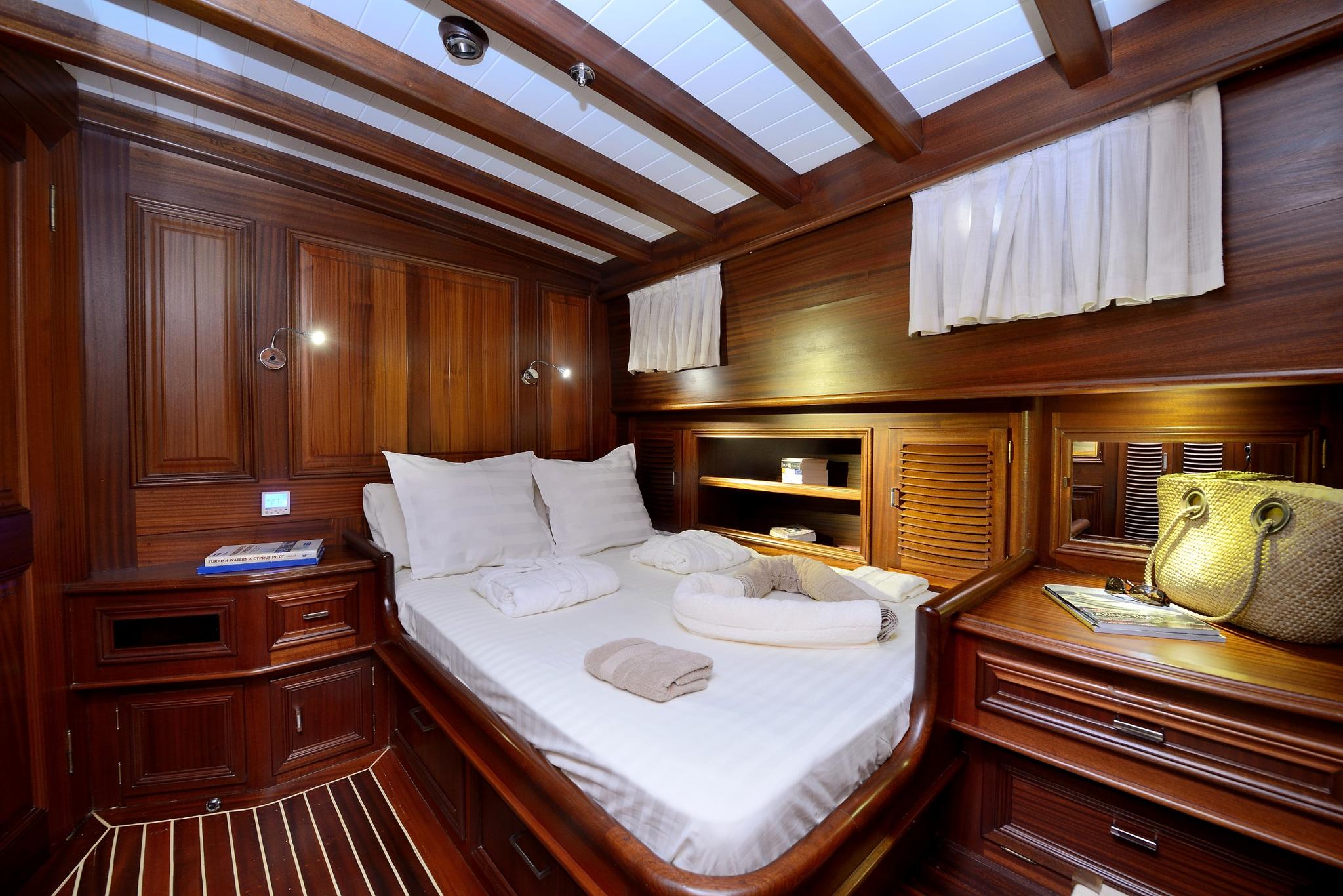 yacht guest cabin with double bed, white linens, wooden paneling and ceiling windows